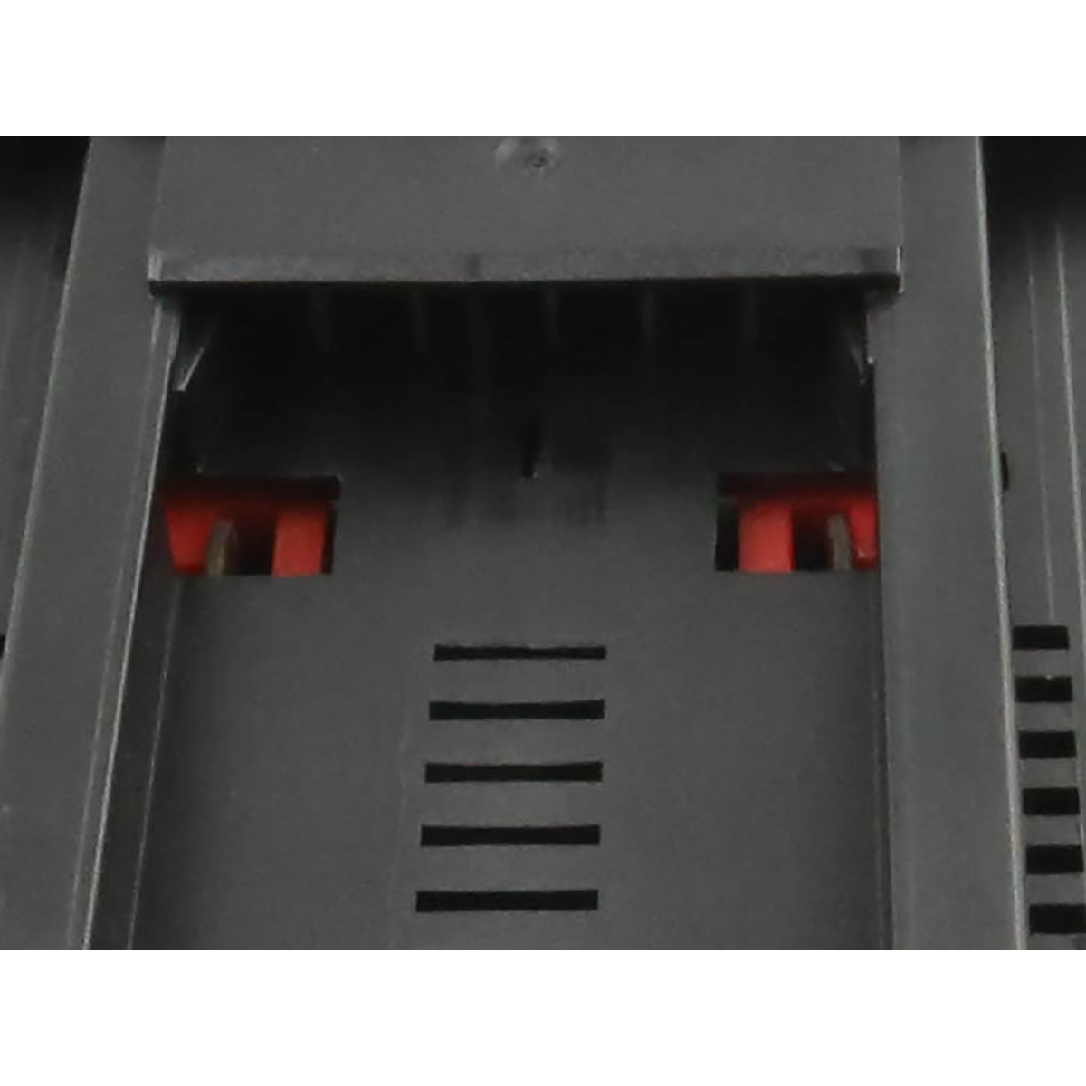 Primo piano di un componente in plastica grigio scuro. Presenta fessure, linguette rosse e linee orizzontali. Lo sfondo è in plastica simile.