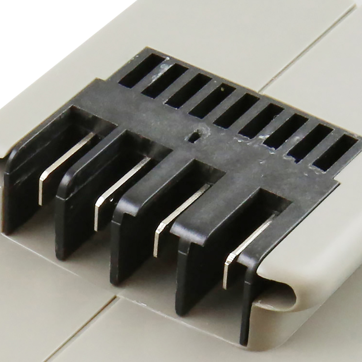 Primo piano di un componente in plastica grigia con alette nere scanalate. Elementi metallici argentati visibili tra le alette.
