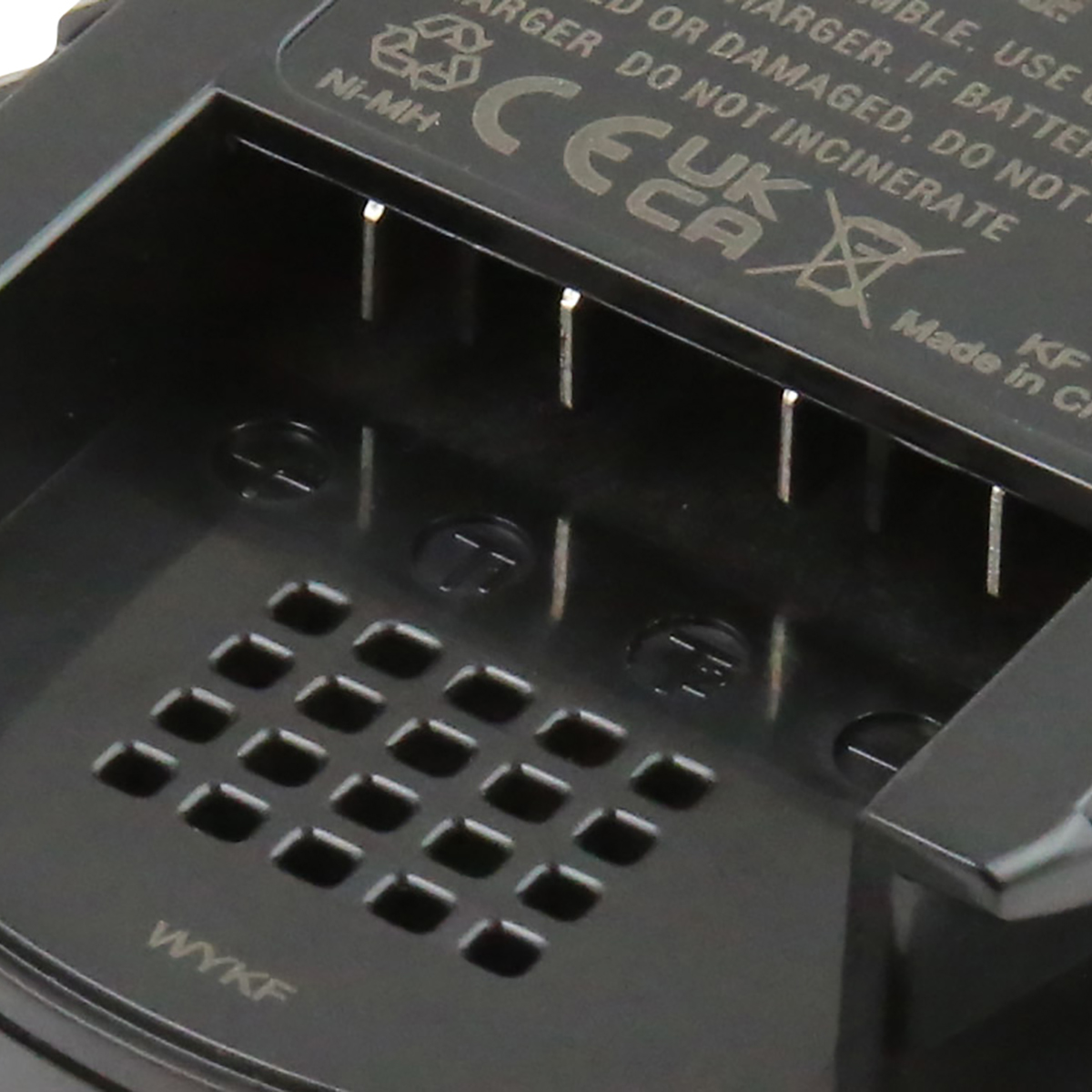 Primo piano di un caricabatterie nero con contatti metallici, fori di ventilazione e testo tra cui 'Ni-MH' e simboli di sicurezza.