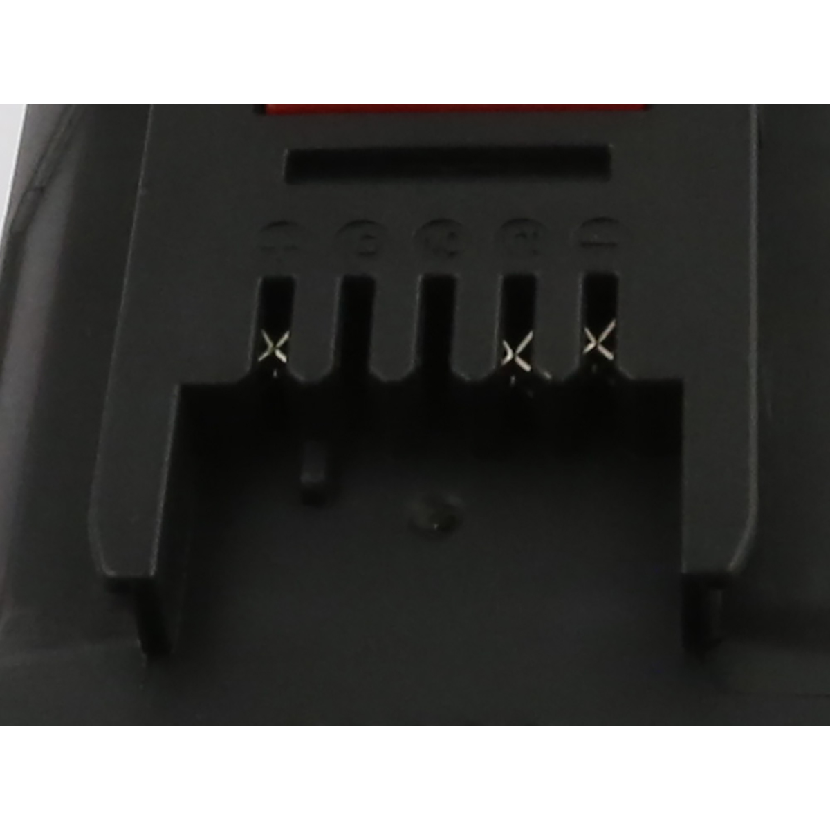 Primo piano di un componente in plastica nera con fessure e contatti metallici. Una parte rettangolare rossa è visibile nella parte superiore.