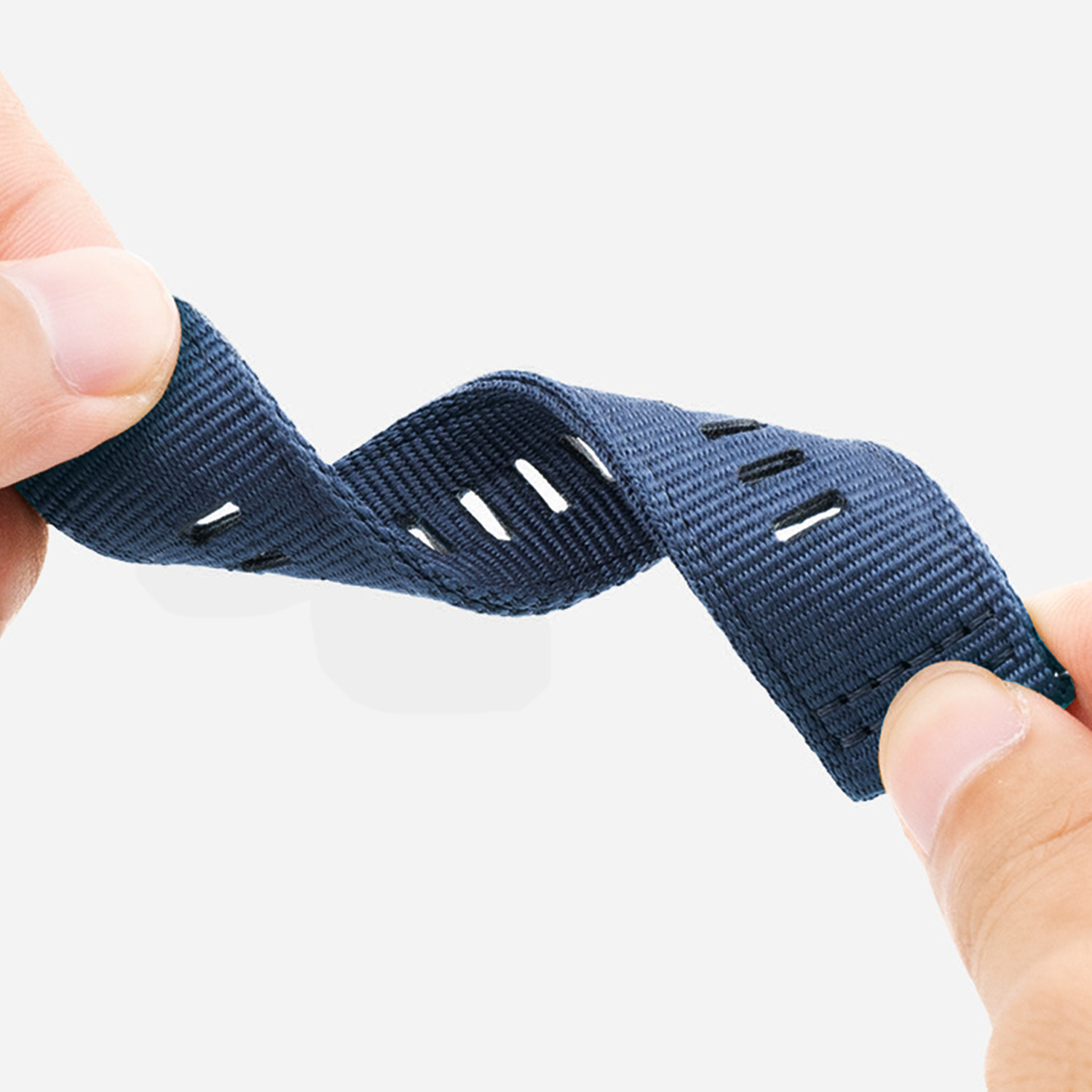 Mani che tengono un cinturino in tessuto blu scuro con fori. Il cinturino è leggermente piegato, mostrando la sua trama e lo sfondo bianco.