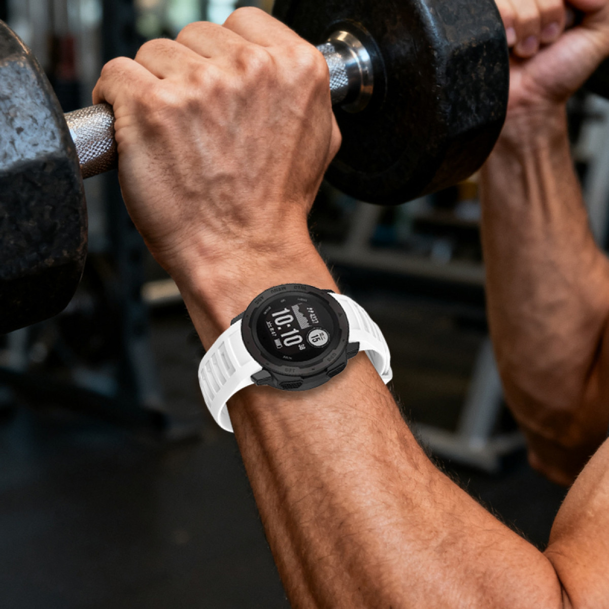 Mann hebt Hantel, trägt Smartwatch mit weißem Band. Fitnessstudio-Umgebung im Hintergrund sichtbar.