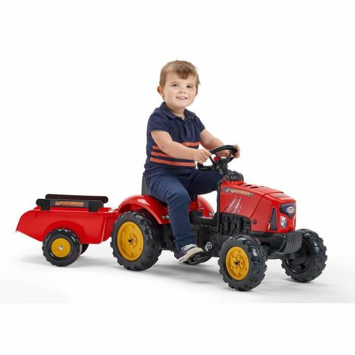 Ein kleiner Junge in blauem Hemd und Jeans sitzt lächelnd auf einem roten Spielzeugtraktor mit Anhänger. Der Traktor hat gelbe Räder.
