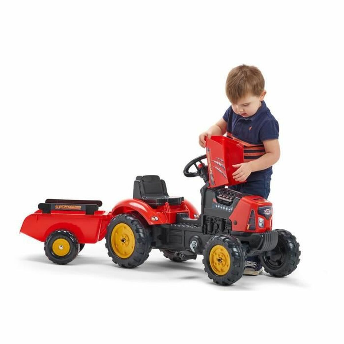 Ein Kind spielt mit einem roten Spielzeugtraktor und Anhänger. Der Traktor hat gelbe Räder. Das Kind hält ein rotes Objekt.