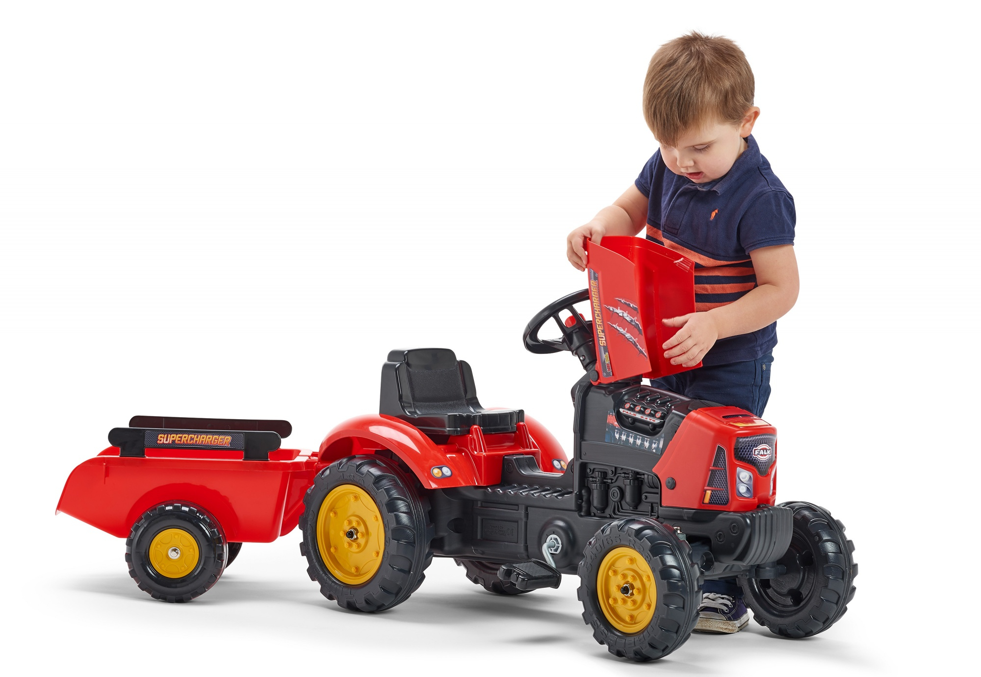 Ein kleiner Junge interagiert mit einem roten Spielzeugtraktor. Der Traktor hat einen Anhänger und der Junge öffnet ein Fach auf der Motorhaube.
