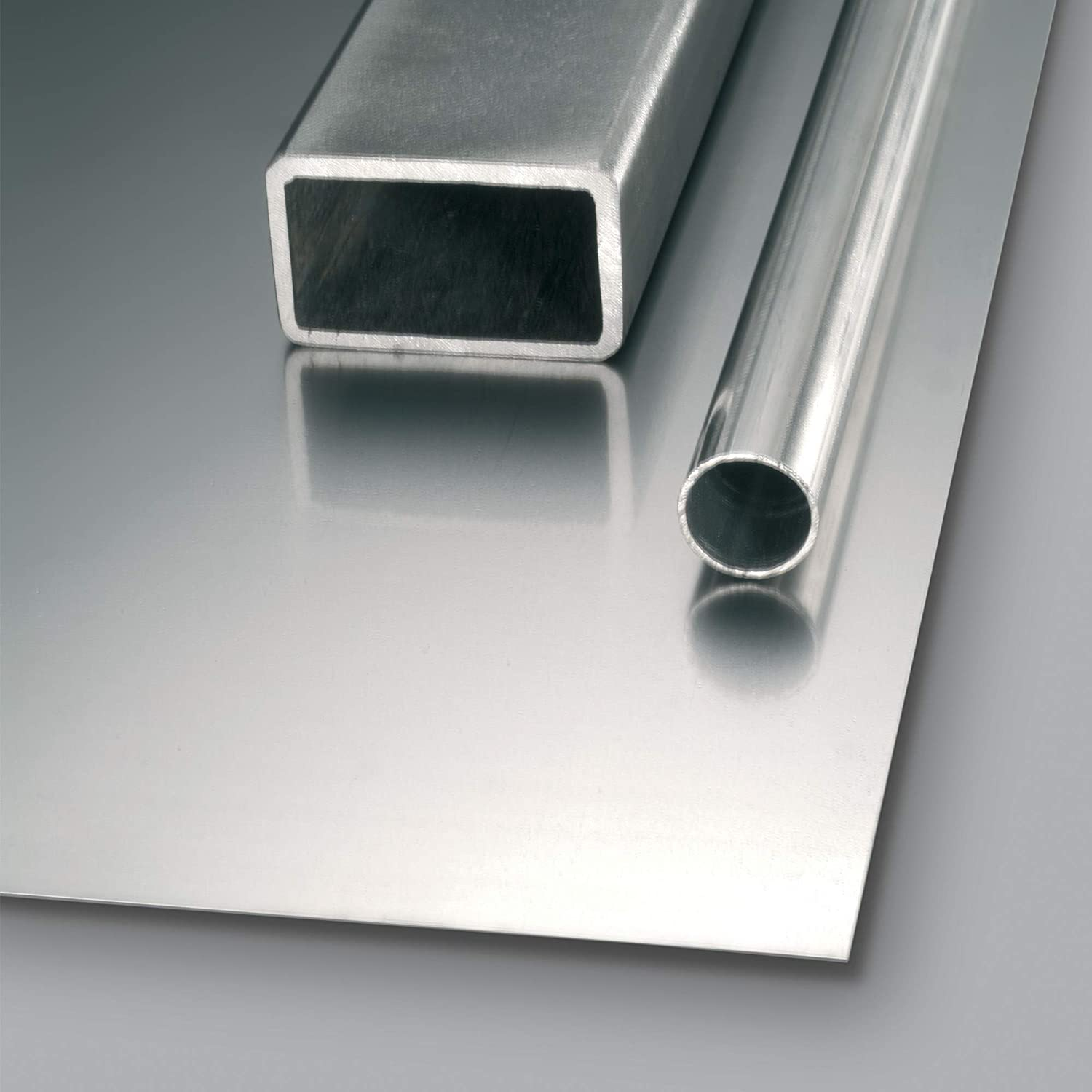 Ein Stahlblech mit einem rechteckigen und einem runden Rohr. Die Objekte sind metallgrau und befinden sich auf einer grauen Oberfläche.