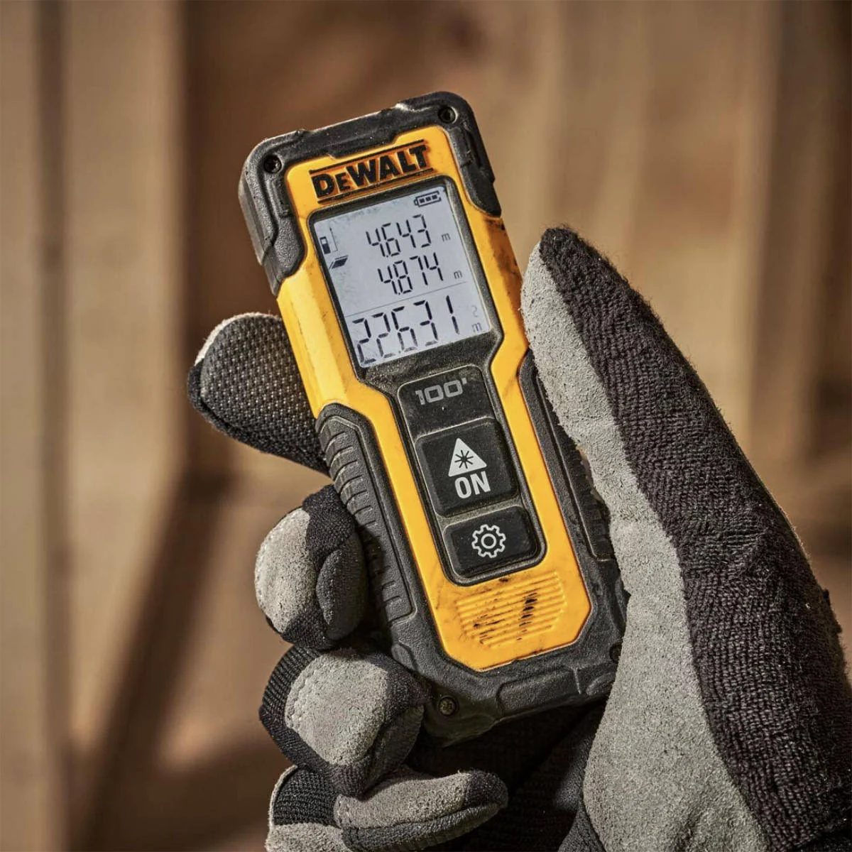 Eine Hand in einem Arbeitshandschuh hält ein gelb-schwarzes DeWalt-Laser-Entfernungsmessgerät. Der Bildschirm zeigt Messwerte an.