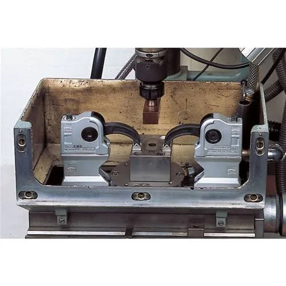 Nahaufnahme von Maschinen. Zwei Metallklammern befinden sich im Vordergrund. Eine Metallbox umgibt die Klammern.