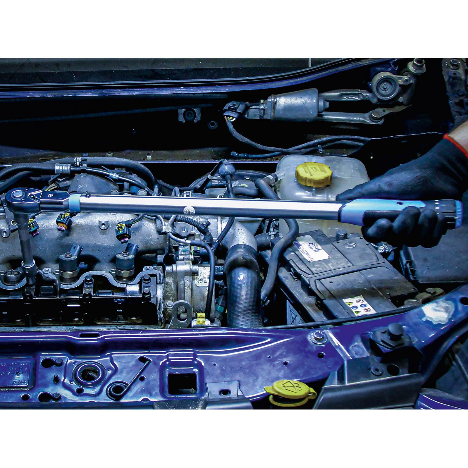 Ein Mechaniker verwendet einen Drehmomentschlüssel an einem Automotor. Der Motor ist sichtbar, mit verschiedenen Komponenten und Drähten.
