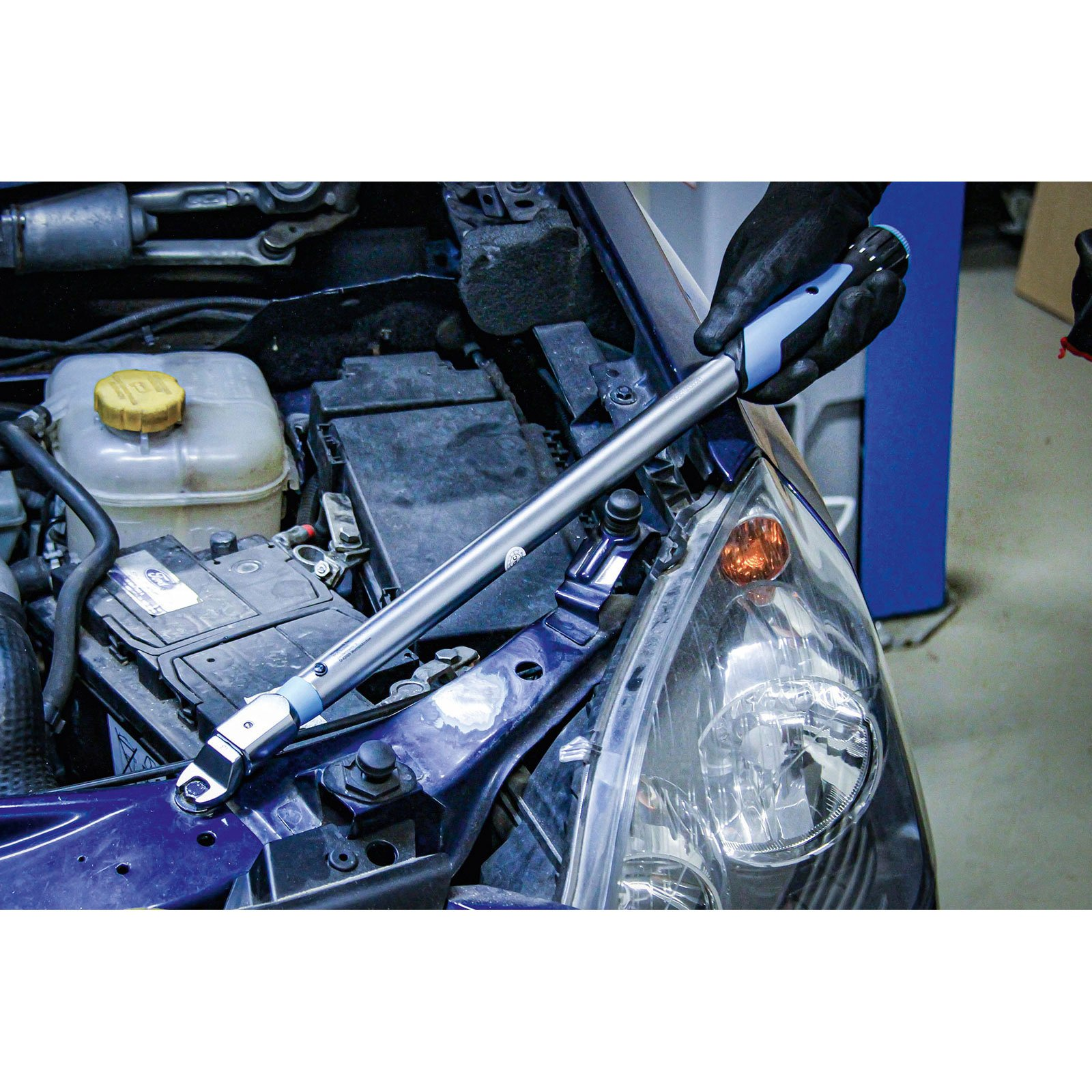 Ein Mechaniker verwendet einen Drehmomentschlüssel an einem Automotor. Die Szene umfasst den Motorraum, den Scheinwerfer und die Batterie des Autos.