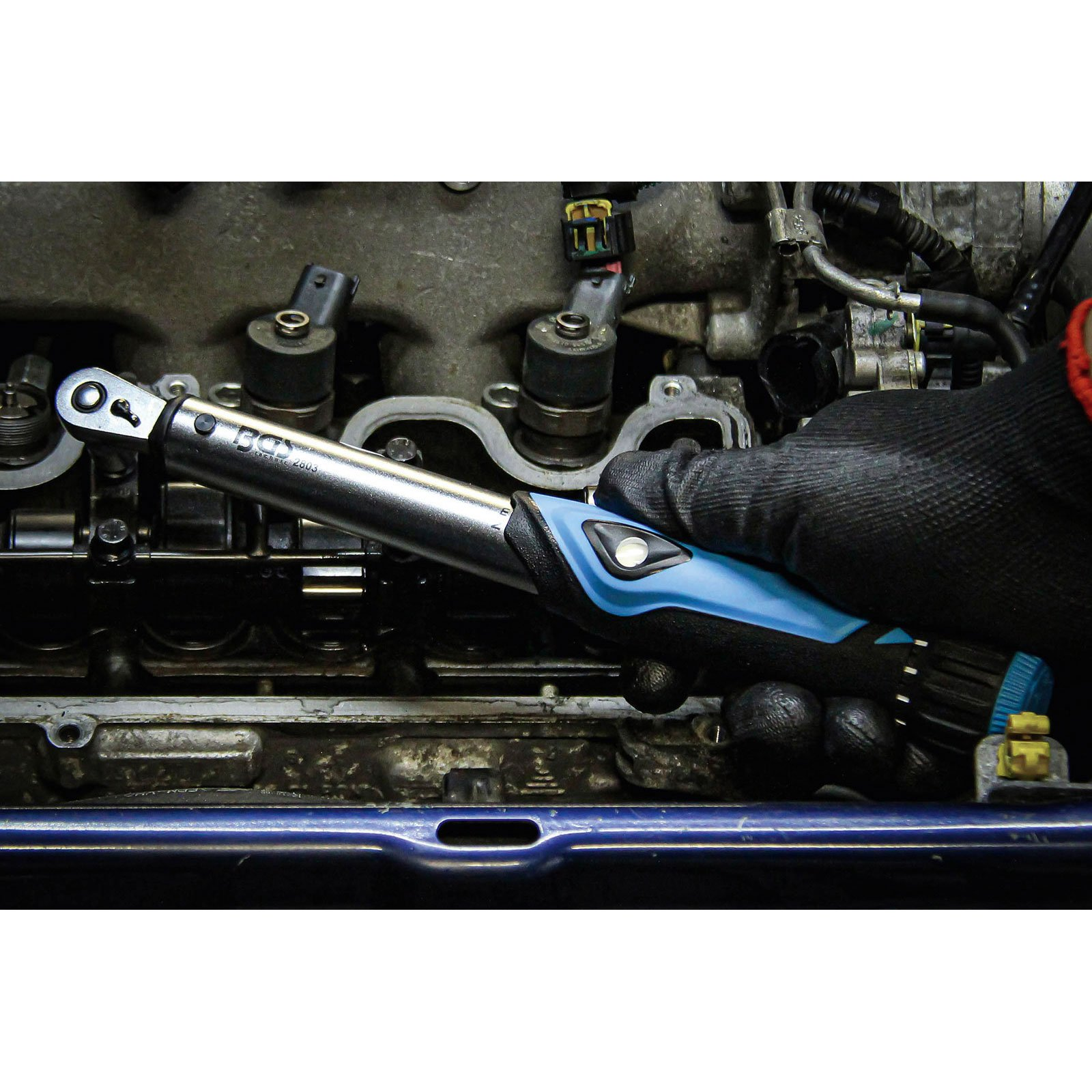 Eine behandschuhte Hand hält einen Drehmomentschlüssel über einem Motor. Der Schraubenschlüssel ist silber und blau. Der Motor ist grau und schwarz.