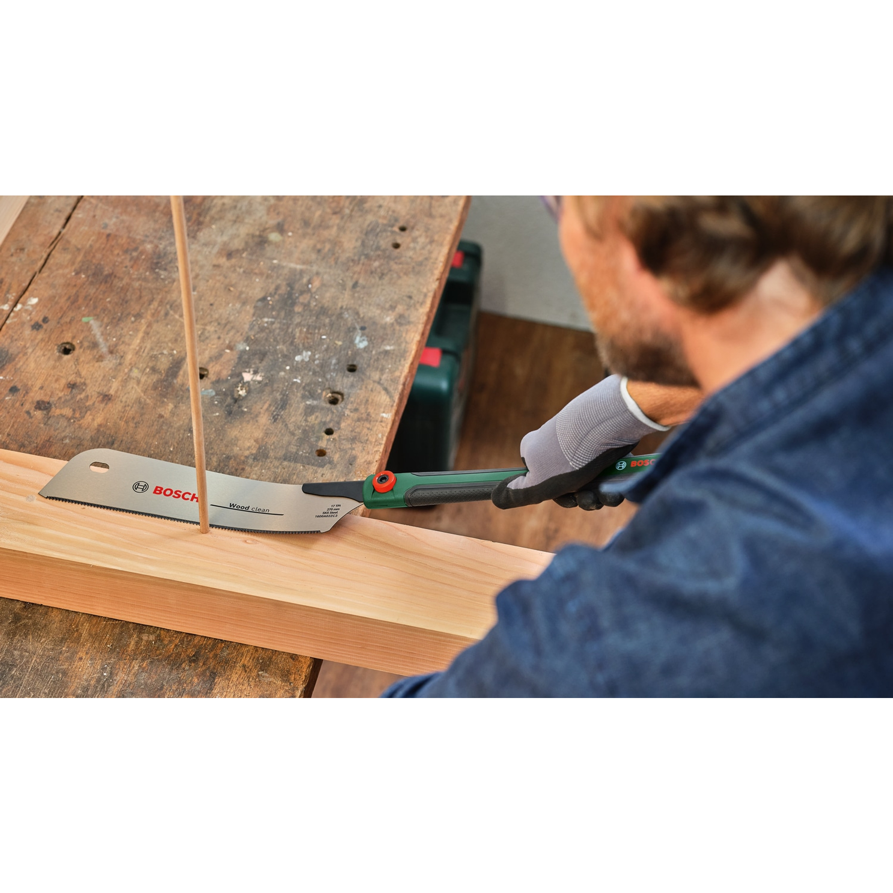 Una persona usa una sega Bosch per tagliare il legno. La sega è tenuta con una mano guantata, tagliando una tavola di legno su un banco da lavoro.