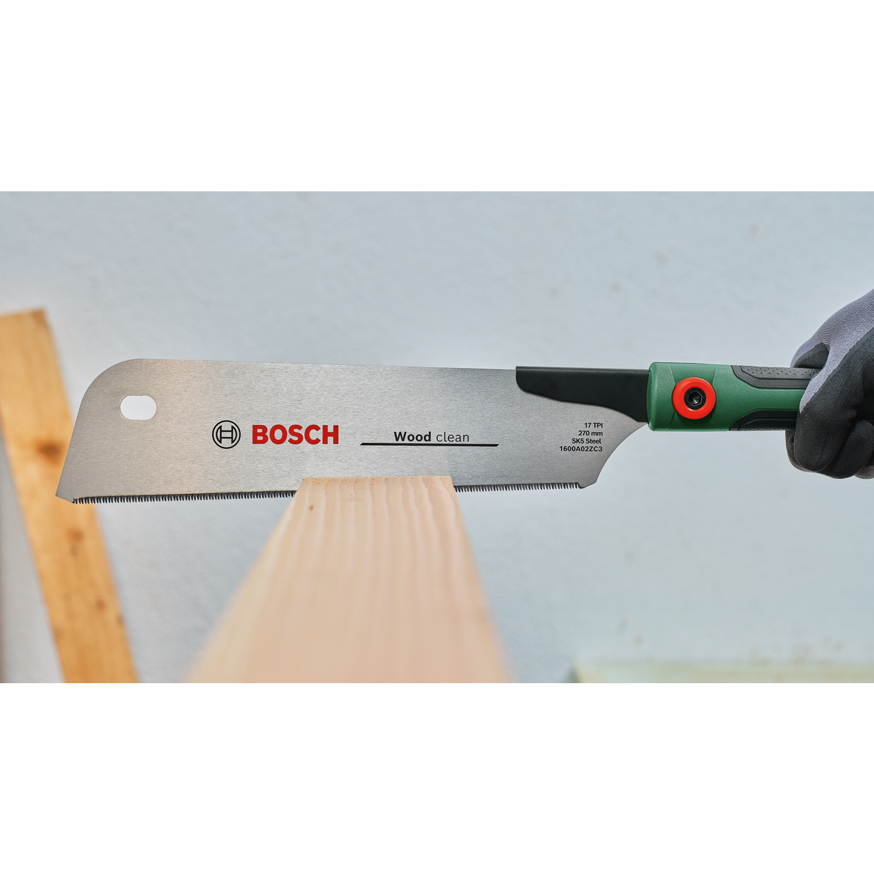 Una sega per legno Bosch taglia un'asse di legno. La sega è tenuta da una mano guantata. La sega ha un manico verde e nero.
