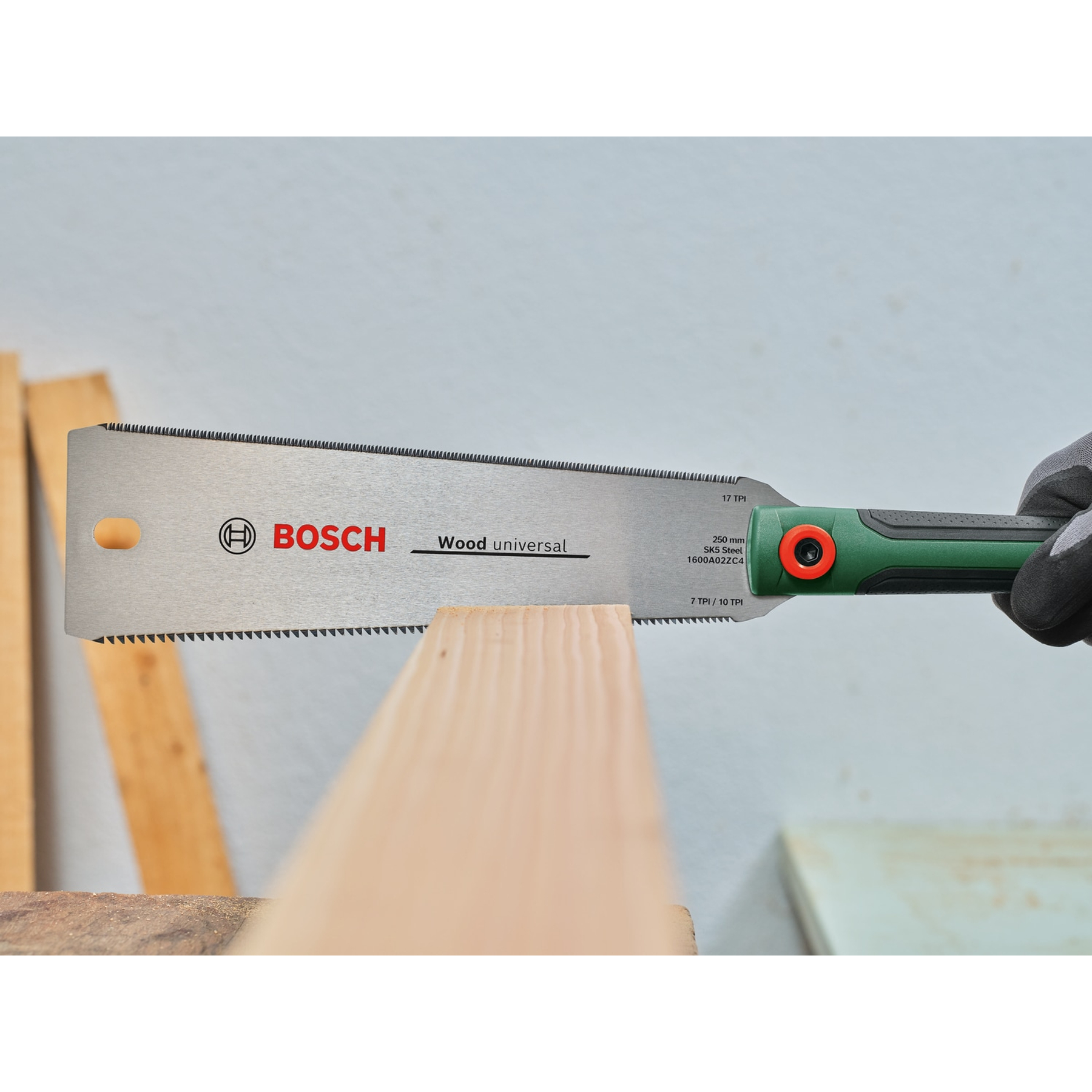 Una sega per legno Bosch è tenuta sopra un'asse di legno. La sega ha un manico verde e nero. La sega è argentata.