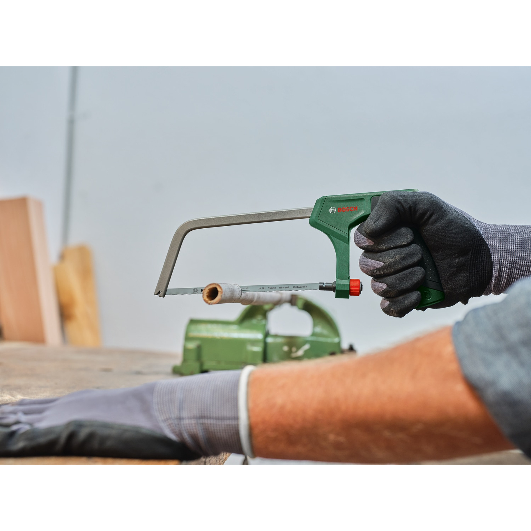 Una persona usa un seghetto alternativo Bosch verde per tagliare un tassello di legno fissato in una morsa.