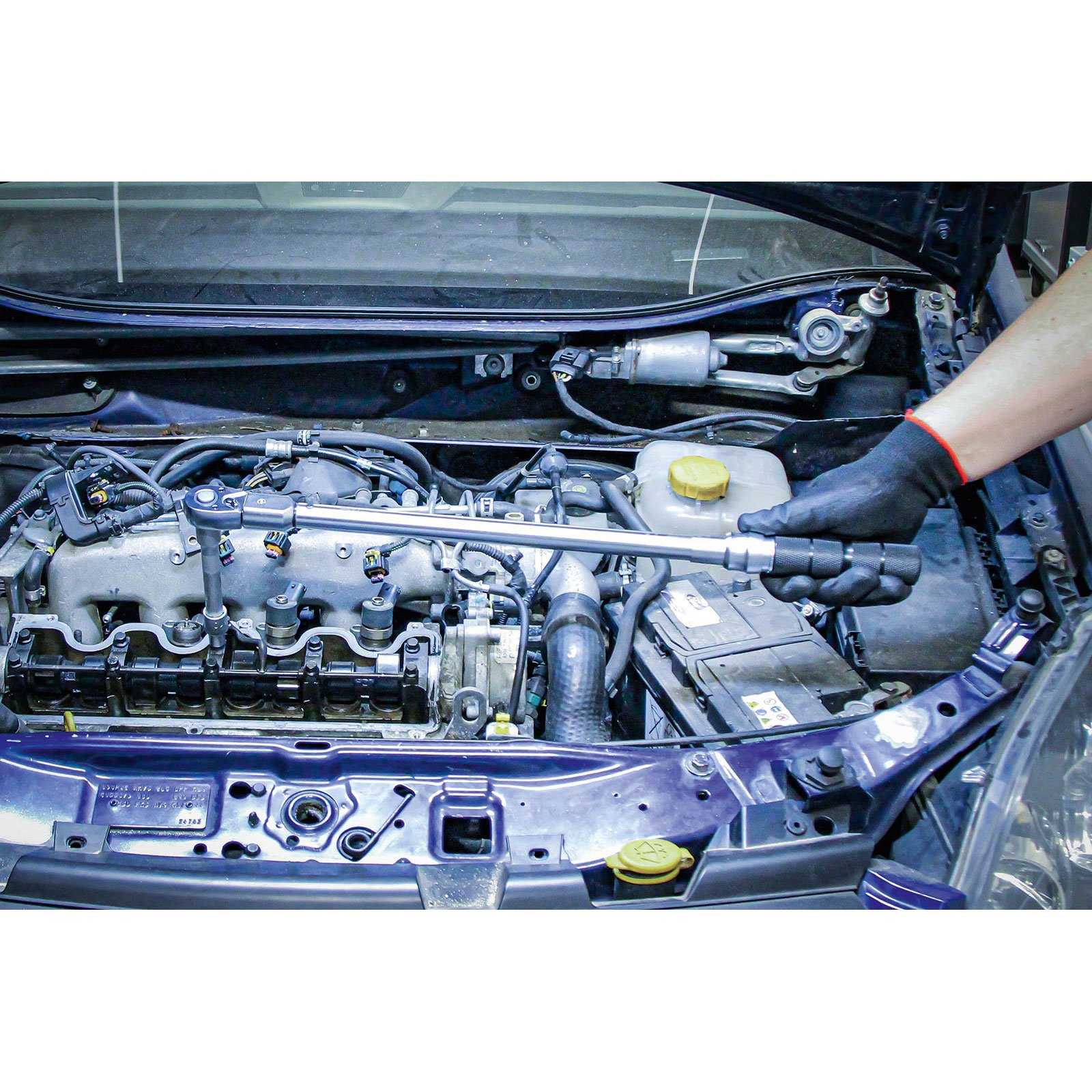 Mechaniker arbeitet an einem Automotor. Er benutzt einen Schraubenschlüssel. Der Motor befindet sich in der Motorhaube und zeigt verschiedene Teile.