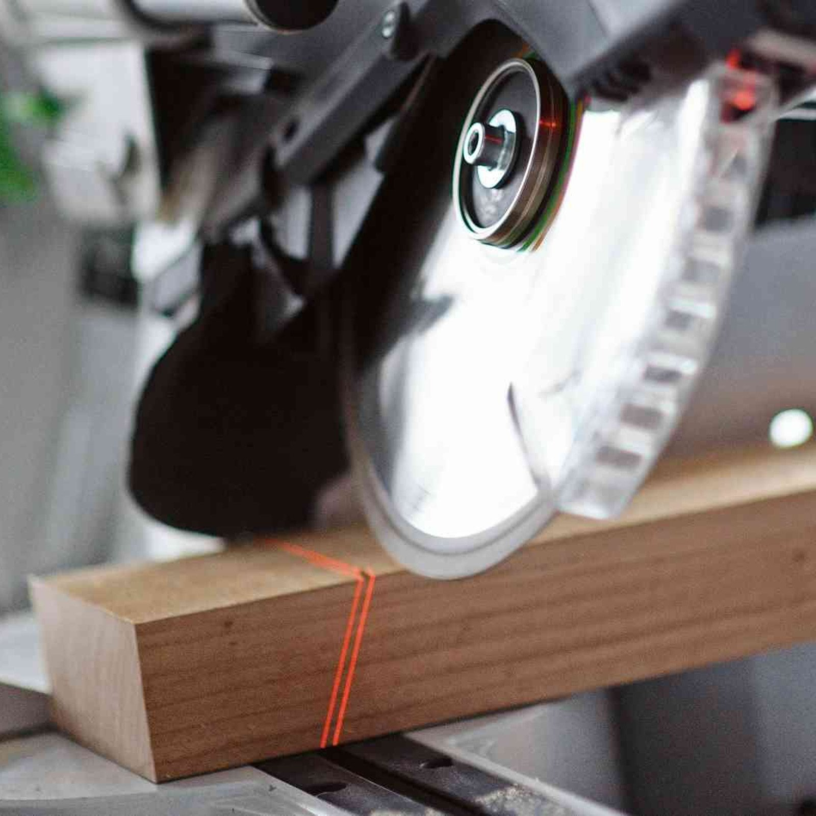 Una sega circolare taglia un blocco di legno. Linee laser rosse guidano il taglio. La lama è visibile.