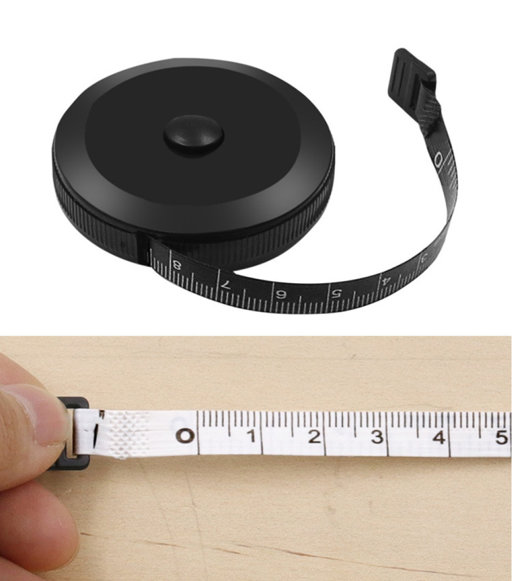 Ein schwarzes Maßband ist teilweise ausgezogen und zeigt Zahlen. Darunter hält eine Hand ein weißes Band mit Zahlen auf einer Holzoberfläche.