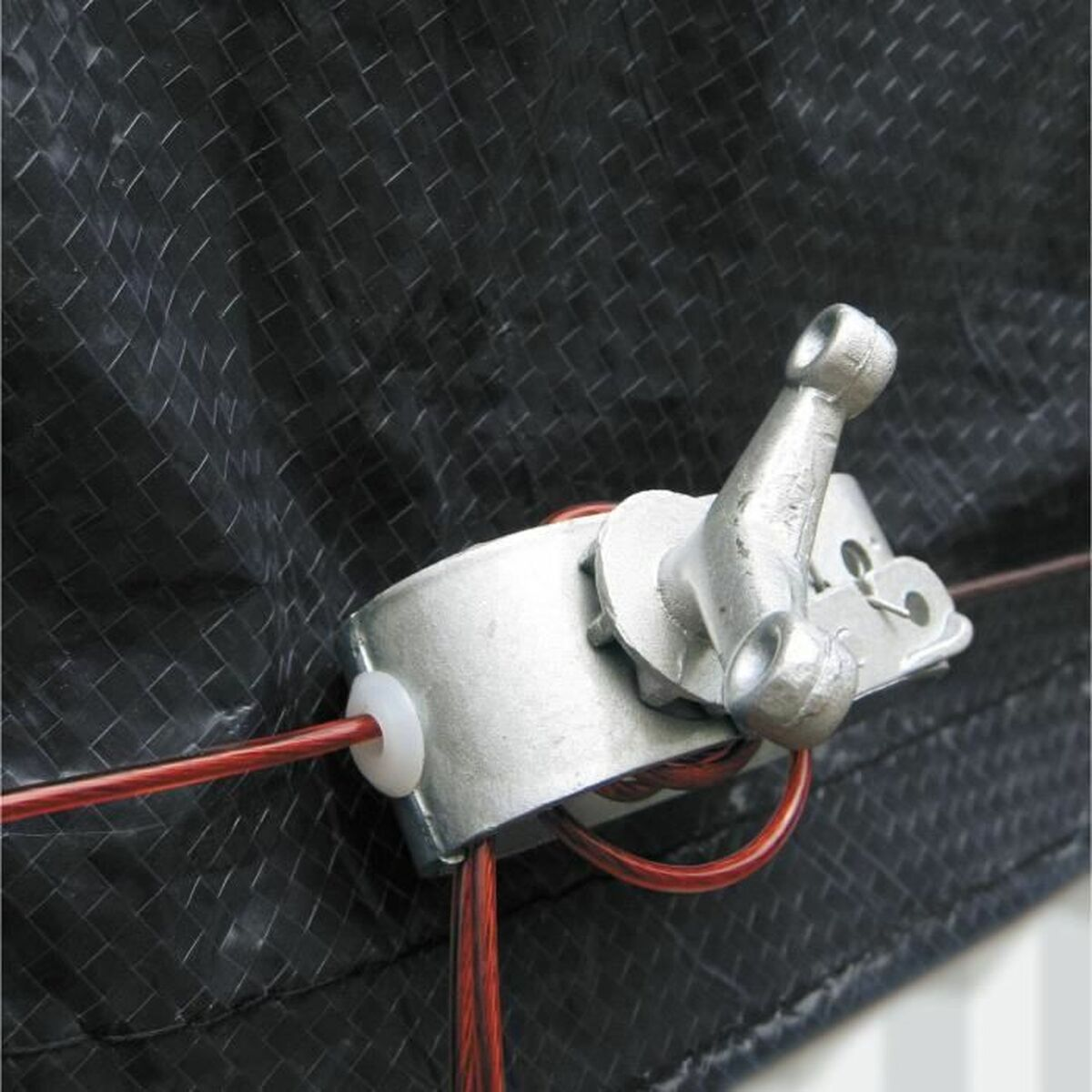 Ein Metallhebel und eine Klemme sichern rote Drähte vor einem schwarzen, gewebten Hintergrund. Der Hebel ist silberfarben, die Drähte sind rot.