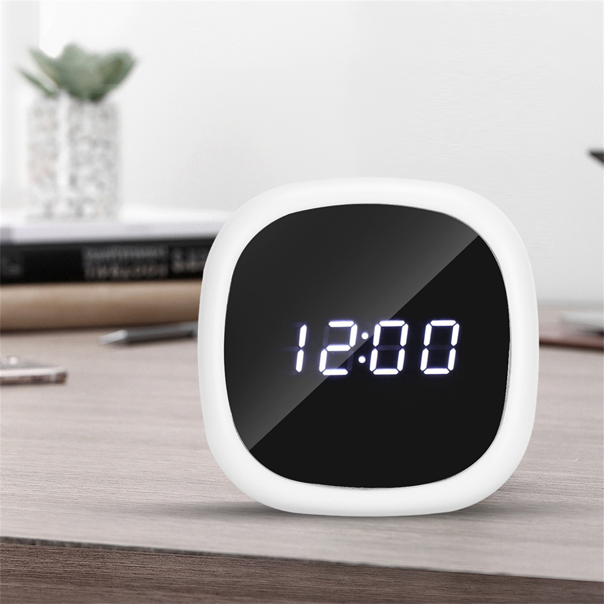 Eine Digitaluhr, die 12:00 Uhr auf einem schwarzen Bildschirm anzeigt. Sie hat einen weißen, abgerundeten Rahmen und steht auf Holz.
