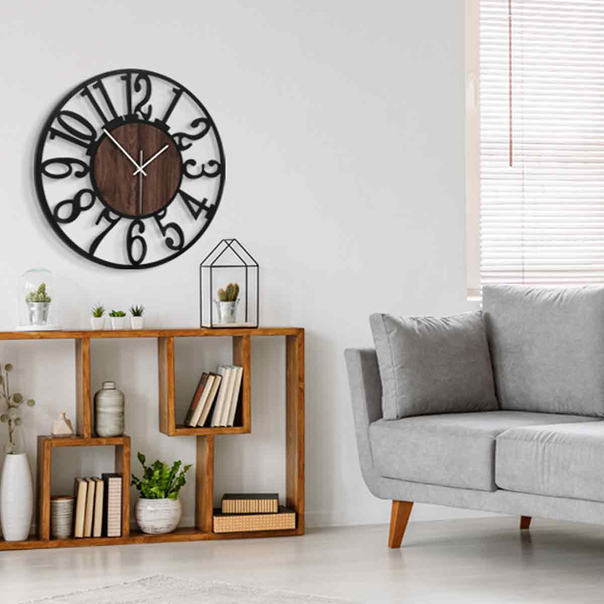 Ein Wohnzimmer mit Wanduhr, Holzregal mit Deko, grauem Sofa und Fenster mit Jalousien. Der Gesamteindruck ist neutral.