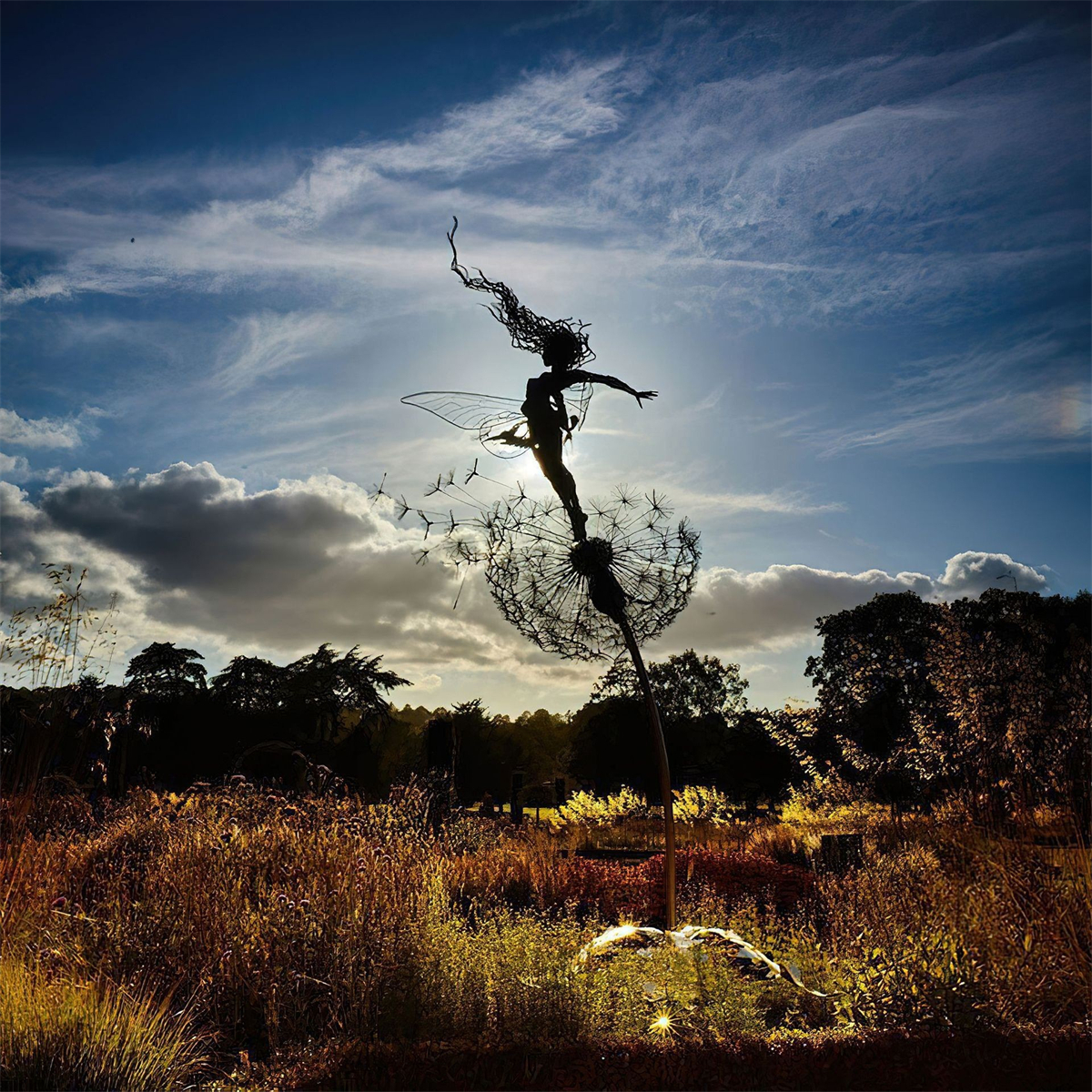 Silhouette einer Fee auf einem Löwenzahn vor hellem Himmel. Löwenzahnsamen fliegen. Ein Grasfeld im Vordergrund.