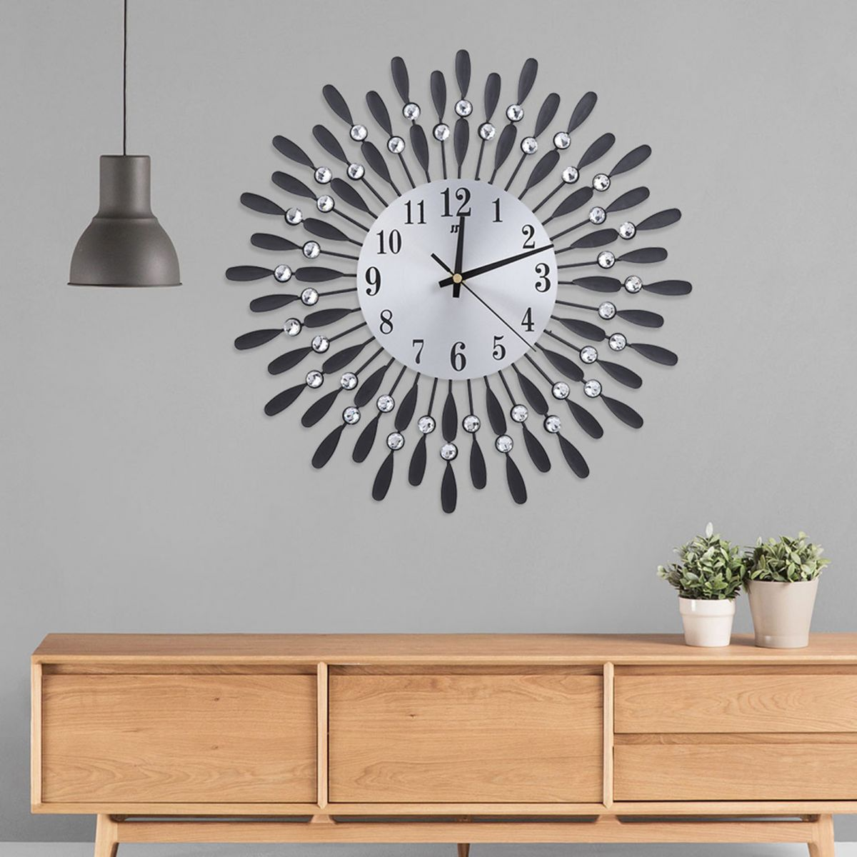 Dekorative Wanduhr mit schwarzen Blütenblättern, silbernem Ziffernblatt und Kristallen. Darunter ein Holzschrank mit Pflanzen.