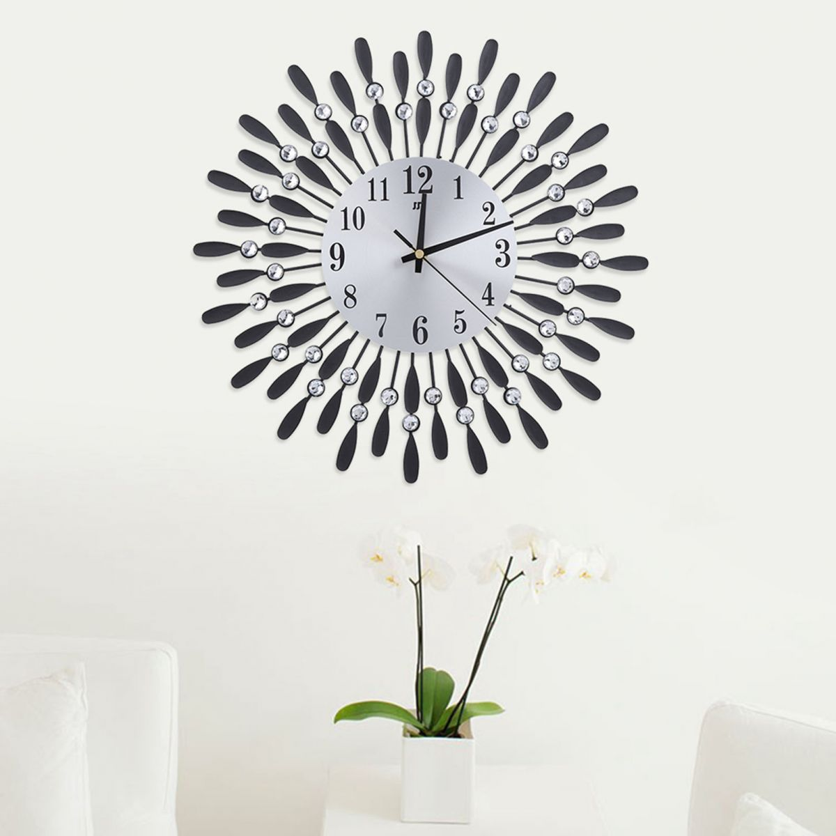 Eine dekorative Wanduhr mit schwarzen Akzenten und Kristallen. Darunter ein weißer Blumentopf mit Orchideen. Weiße Wand und Möbel.