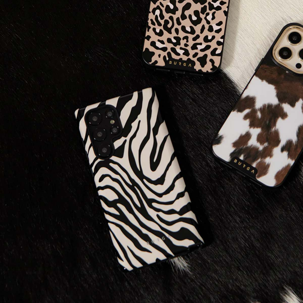 Drie telefoonhoesjes met dierenprints op een zwart-witte vachtachtergrond. Zebra-, luipaard- en koeienprint designs.