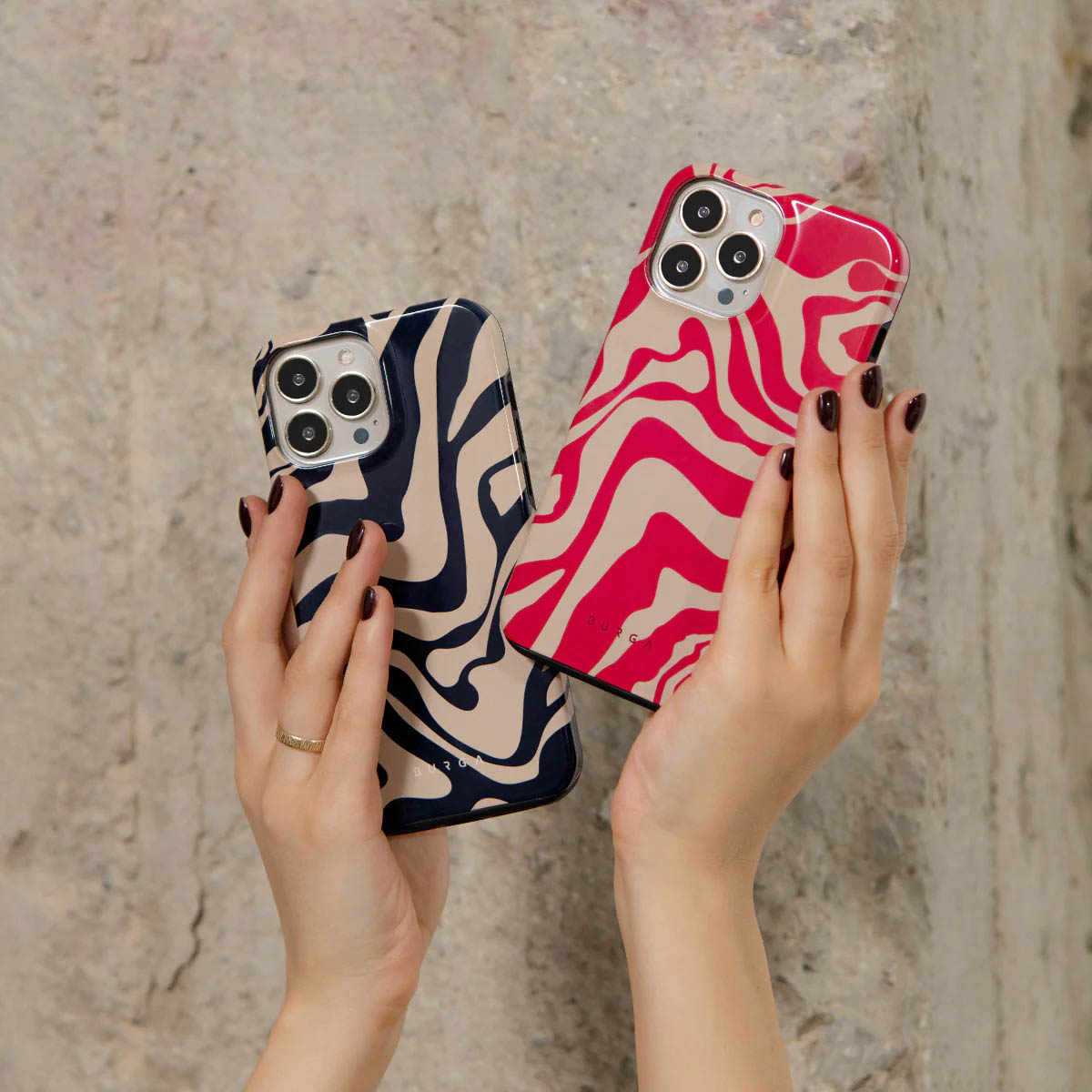 Twee handen houden telefoonhoesjes met zebrapatroon vast. Eén is marineblauw en beige, de andere roze en beige. Een gouden ring is zichtbaar.