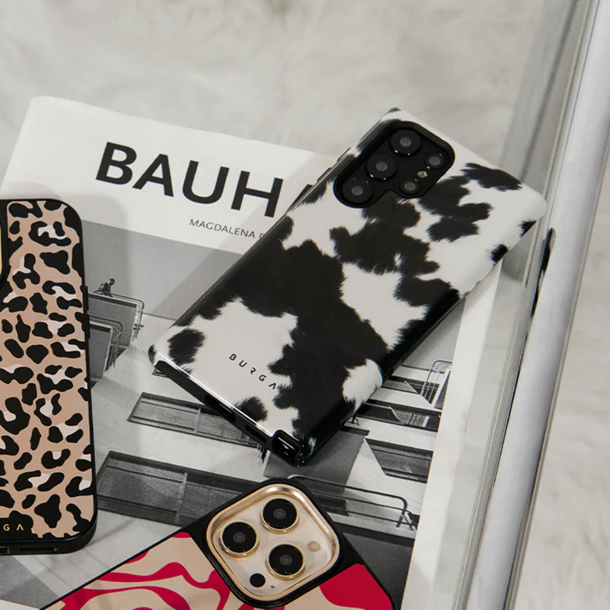 Verschillende telefoonhoesjes op een boek. Eén heeft een koeienpatroon, een andere een luipaardprint. Het boek leest 'BAUHAUS'.