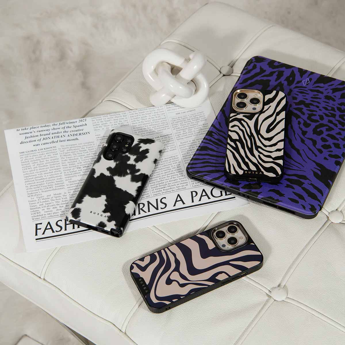 Verschillende telefoonhoesjes met verschillende patronen liggen op een wit oppervlak met een witte decoratieve ketting.