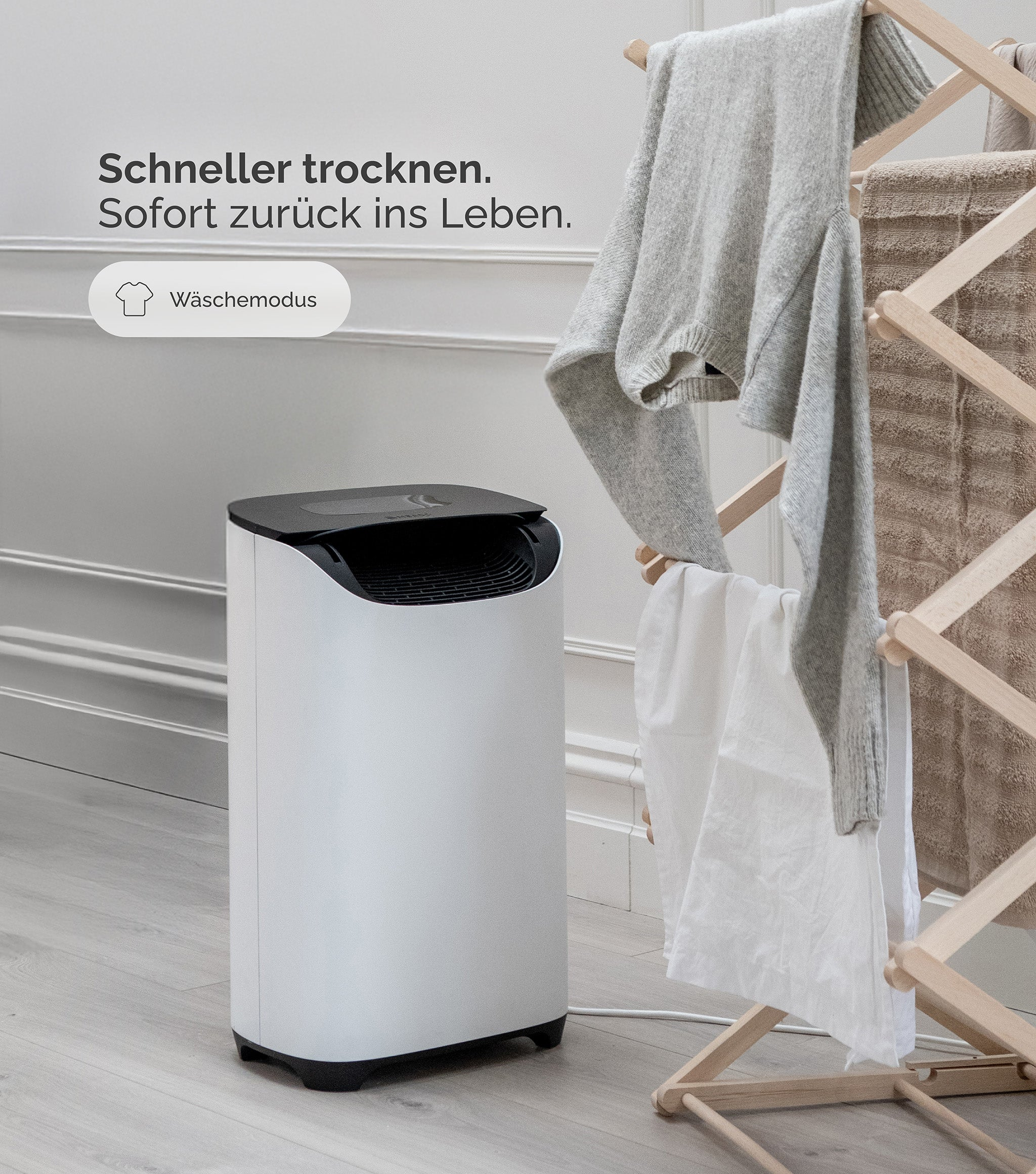 Białe i czarne urządzenie z ubraniami wiszącymi na drewnianym stojaku. Widoczny biały prześcieradło i szary sweter.