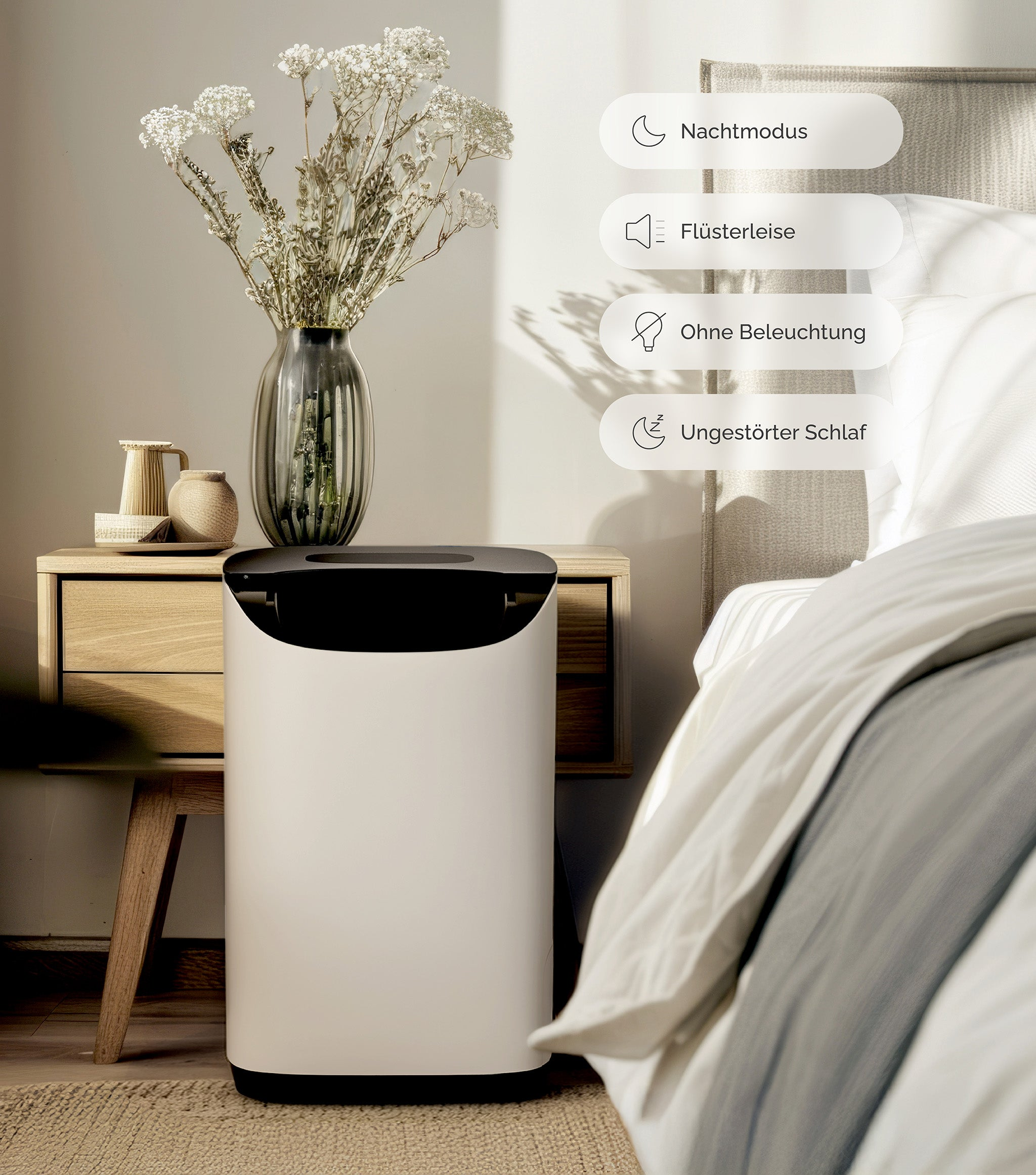 Biały oczyszczacz powietrza obok stolika nocnego z wazonem kwiatów. W tle łóżko.