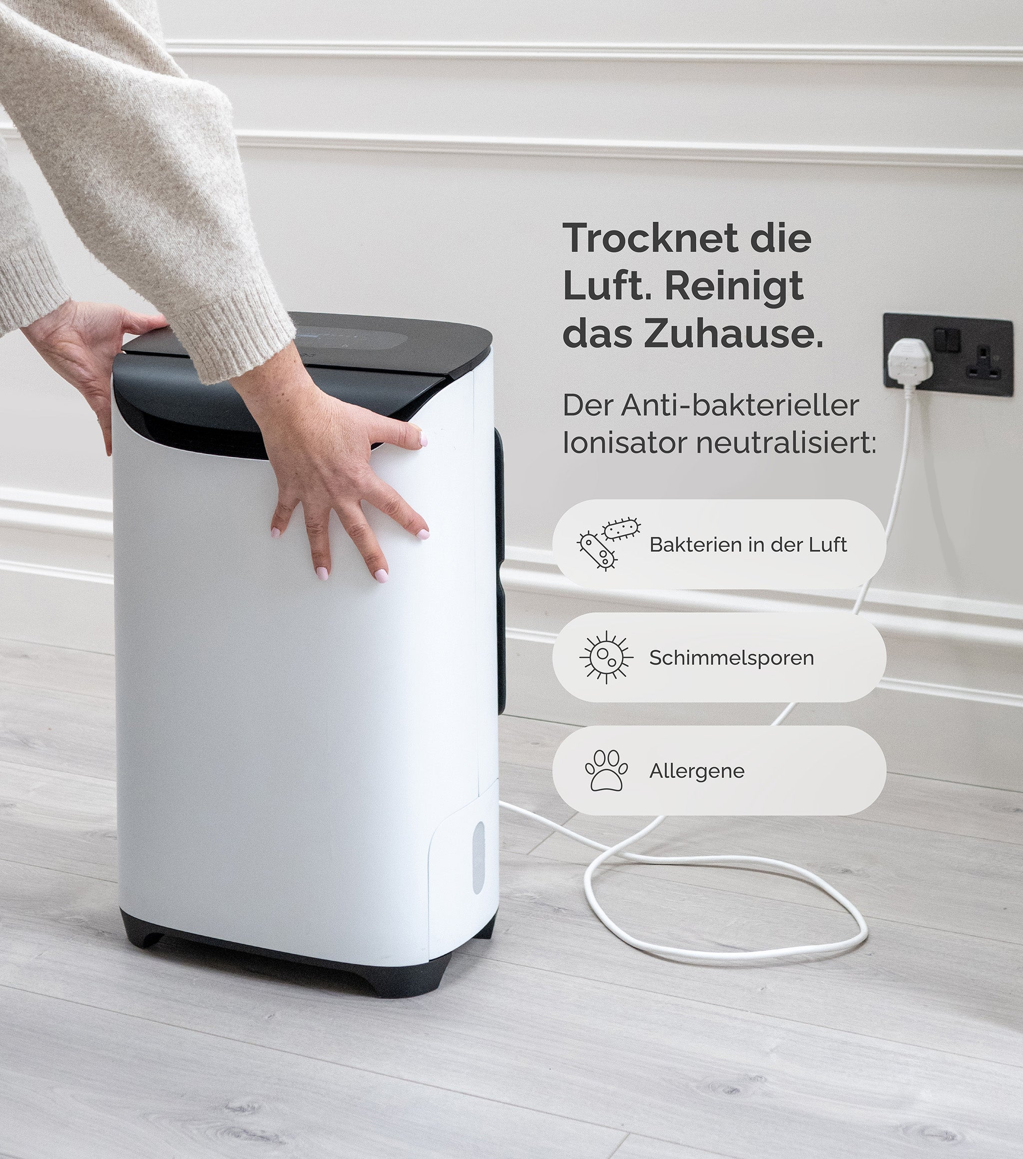 Ręce na białym i czarnym oczyszczaczu powietrza. Tekst mówi, że osusza i oczyszcza powietrze, neutralizując bakterie.