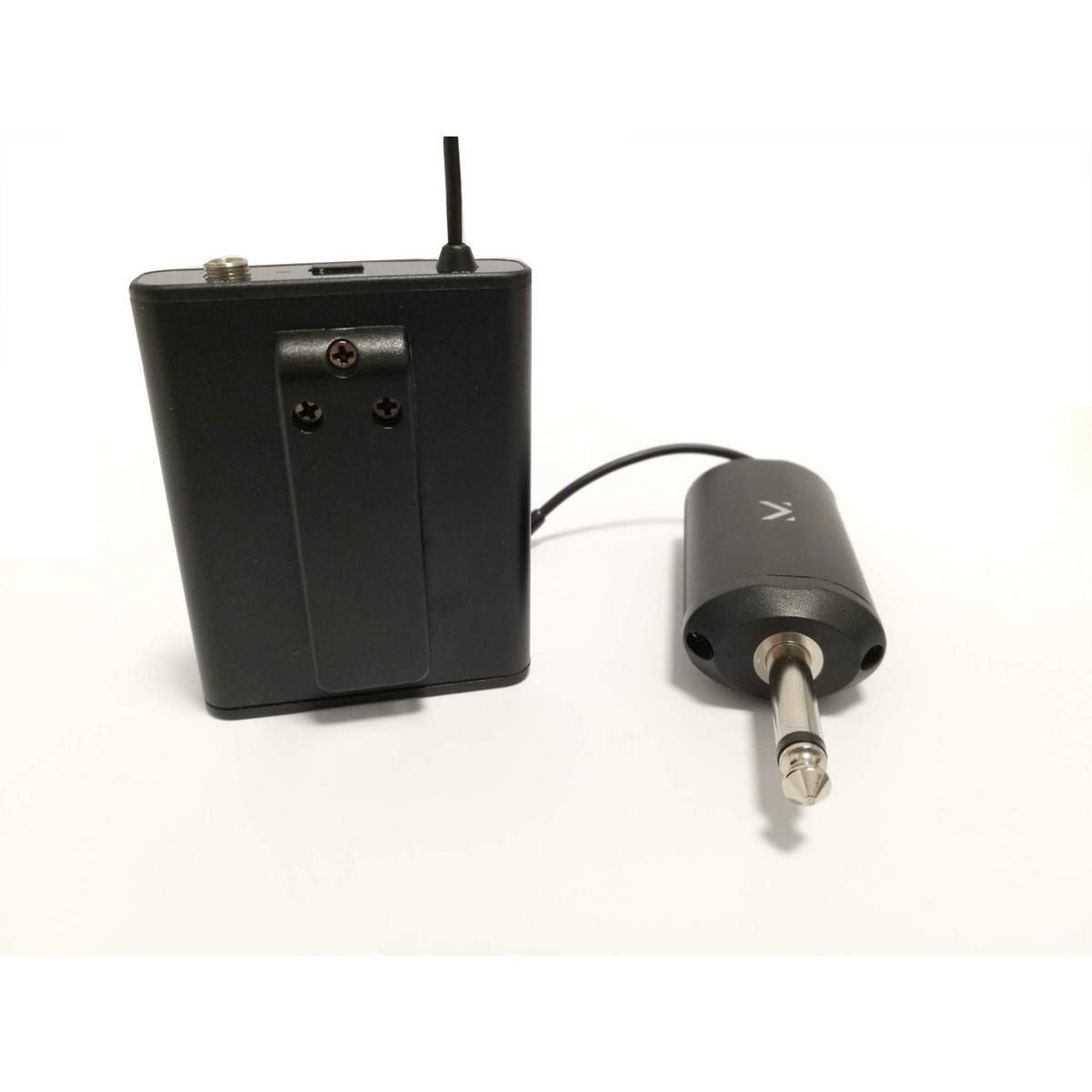 Transmisor de audio negro con antena y receptor conectado con un jack sobre una superficie blanca.
