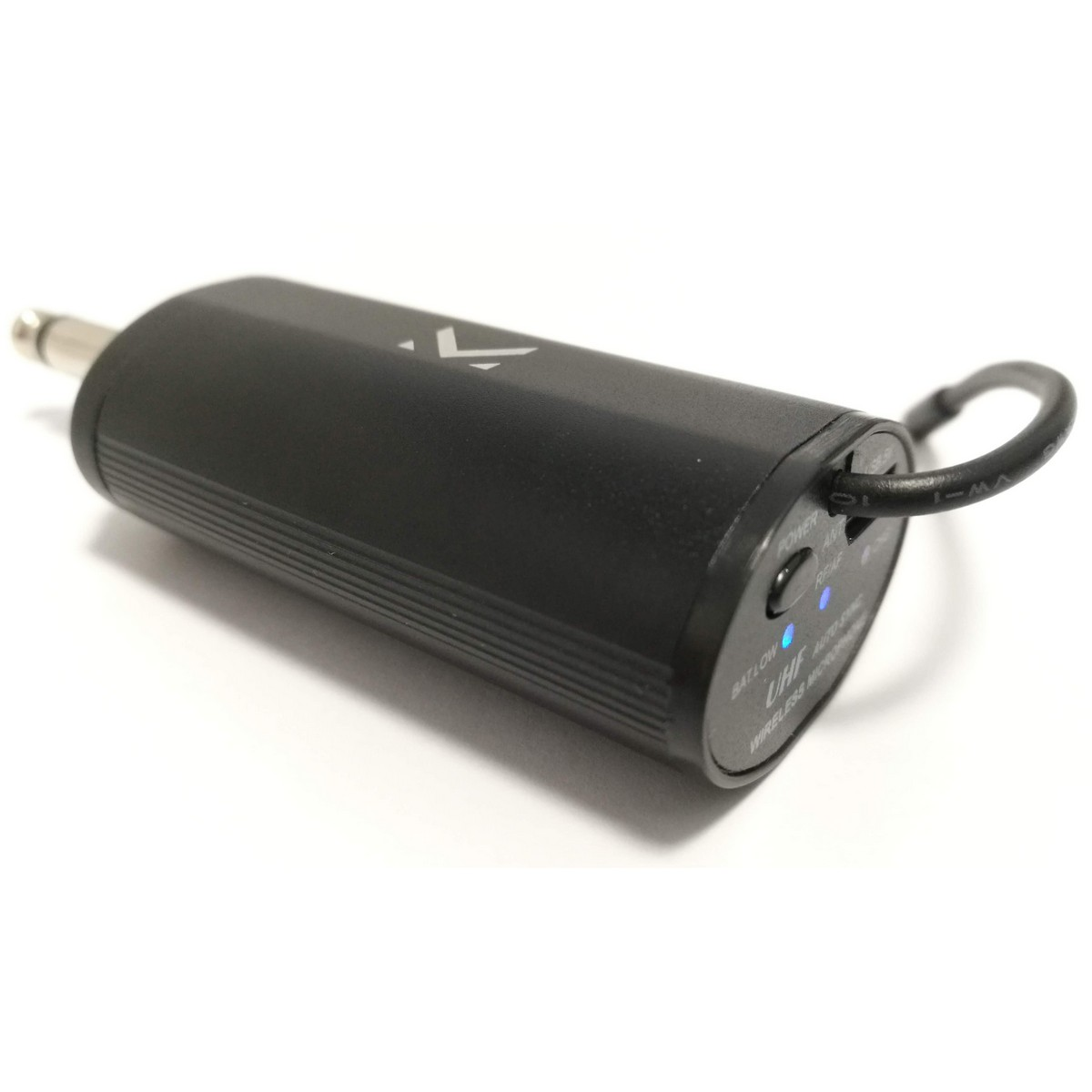 Transmisor de micrófono inalámbrico negro. Tiene un conector jack, un botón de encendido y un cable en bucle. El fondo es blanco.