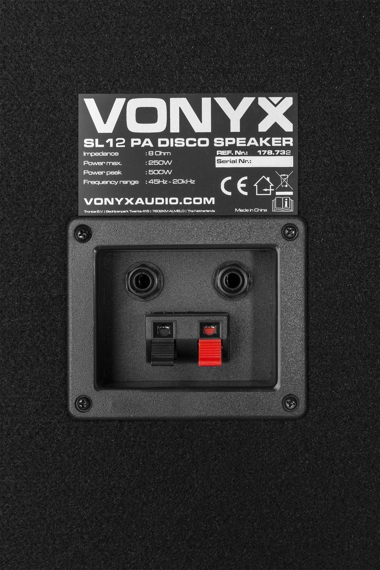 Parte trasera de altavoz negro con texto y puertos de conexión. El texto incluye marca, modelo y especificaciones técnicas. Los puertos son negros y rojos.