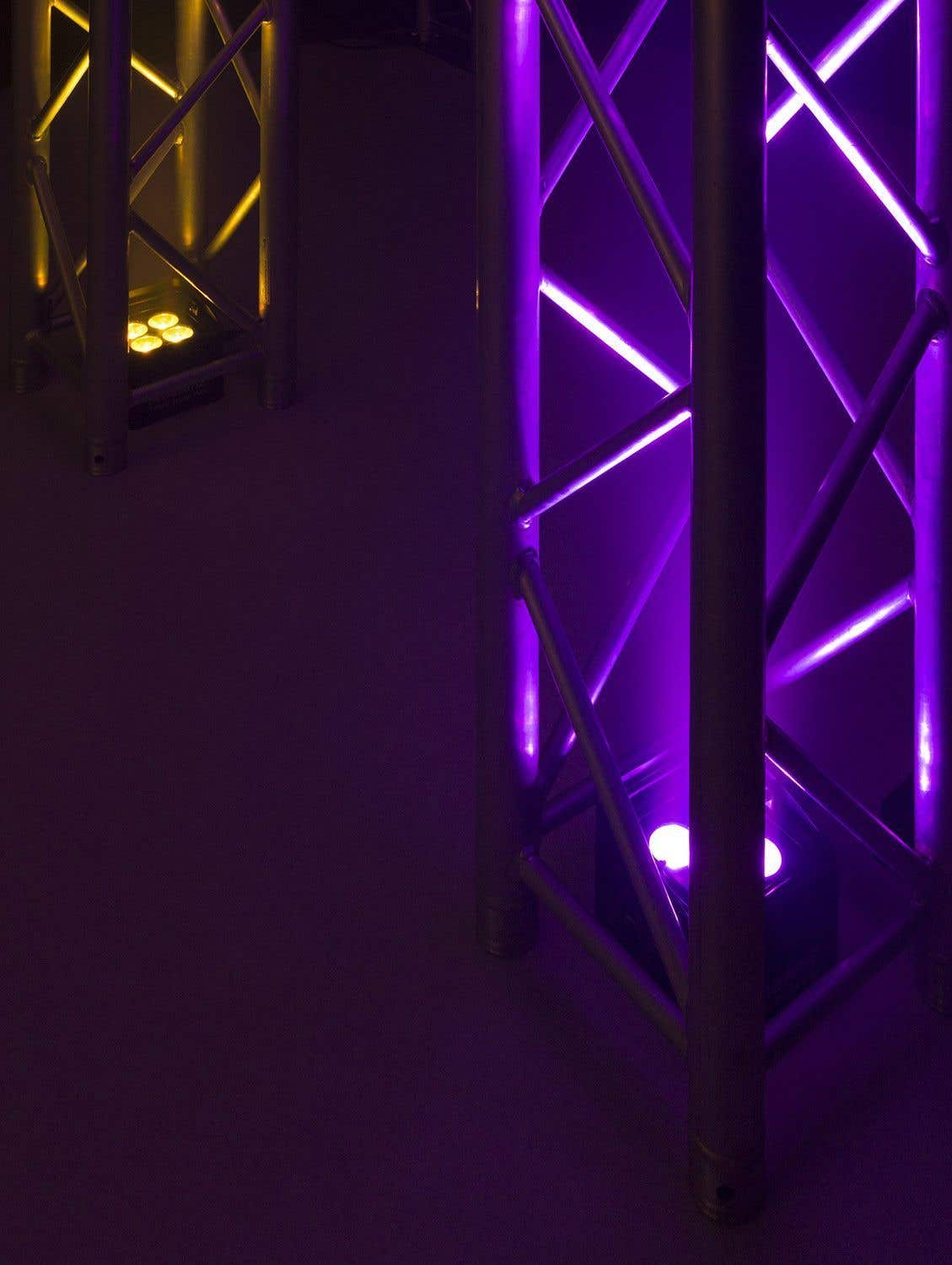 Una estructura de escenario iluminada con luces moradas y amarillas. Las luces iluminan la estructura metálica, creando una escena vibrante y colorida.