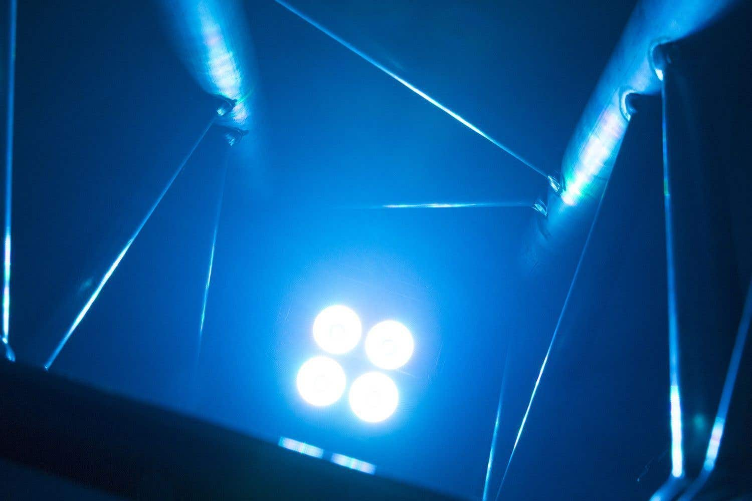Luz azul con cuatro puntos brillantes. Se ven estructuras y líneas metálicas, creando una composición abstracta y moderna.