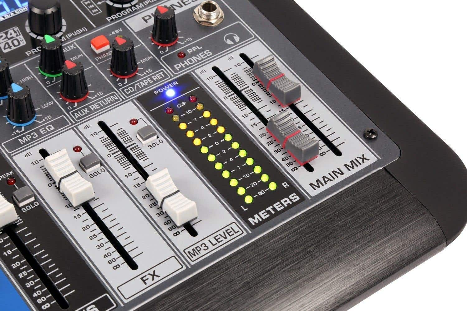 Primer plano de una mesa de mezclas con perillas, faders y medidores. Varios controles están etiquetados, y luces indican los niveles de audio.