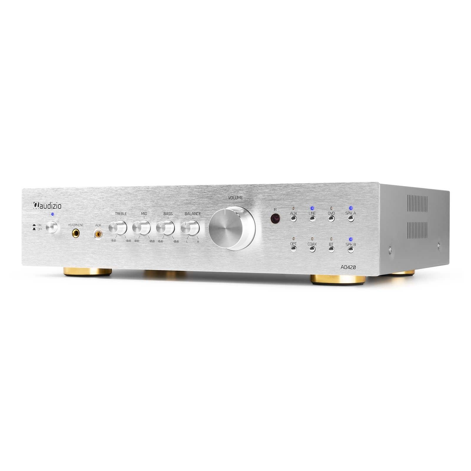 Amplificador de audio plateado con perillas y botones. Control de volumen en el centro. Pies dorados. Luces indicadoras azules.