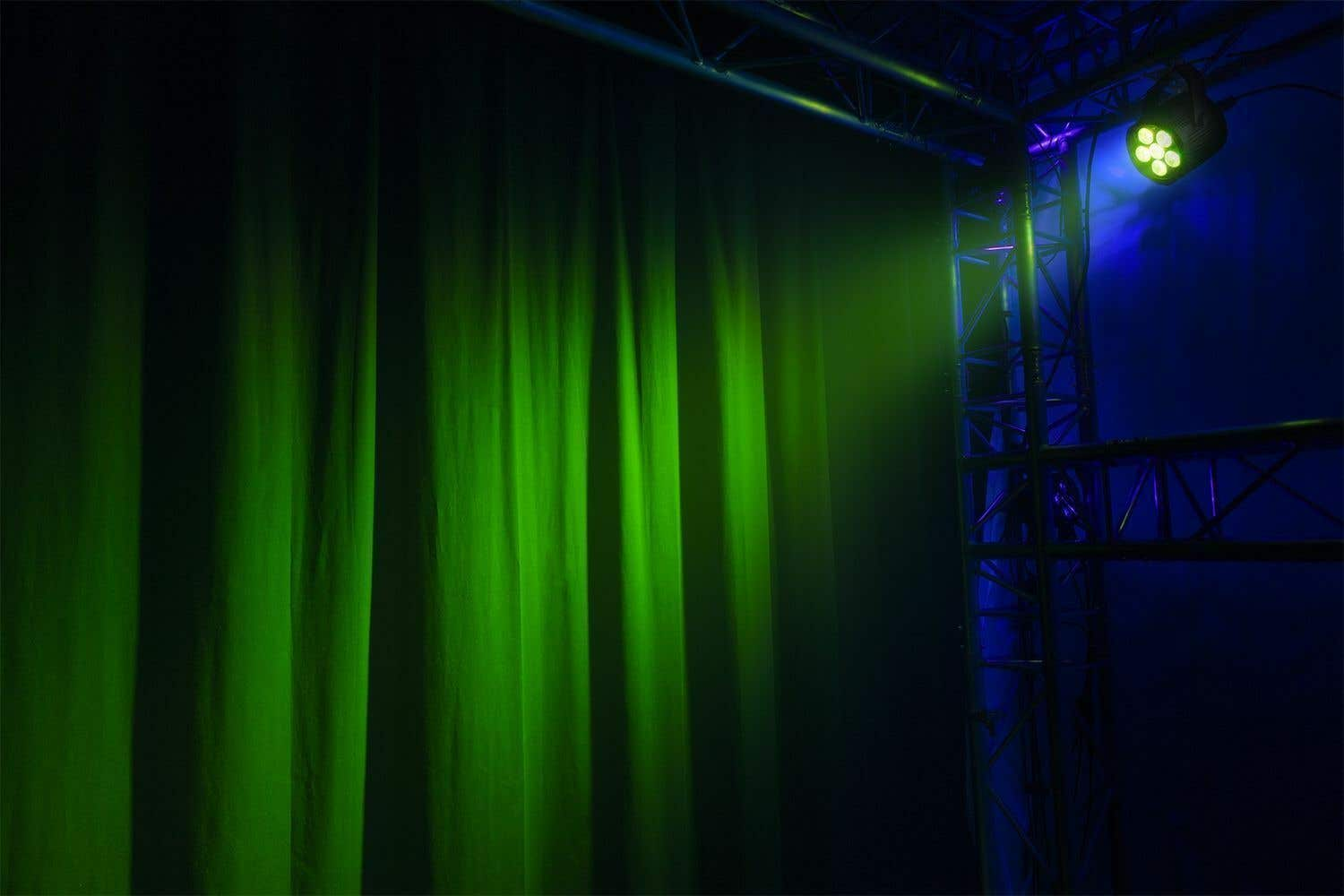 Cortinas verdes iluminadas lateralmente. Estructura metálica a la derecha con foco. Fondo azul.