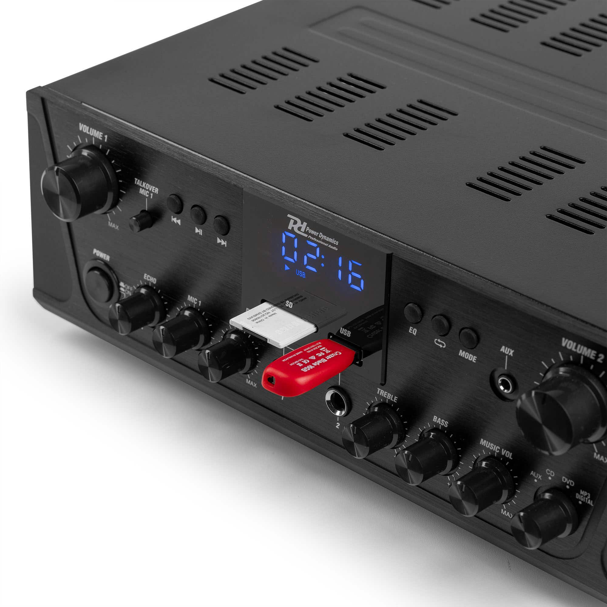 Schwarzer Audioverstärker mit Knöpfen, Tasten und Anschlüssen. Ein roter USB-Stick und eine Digitalanzeige mit der Uhrzeit sind sichtbar.