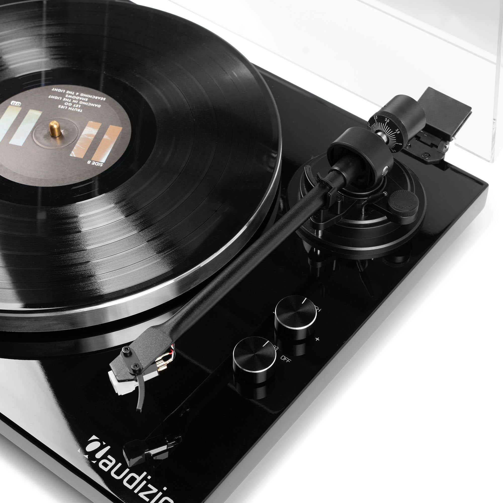 Un tocadiscos negro con un disco de vinilo. El brazo fonocaptor está sobre el disco. Controles en la parte delantera.