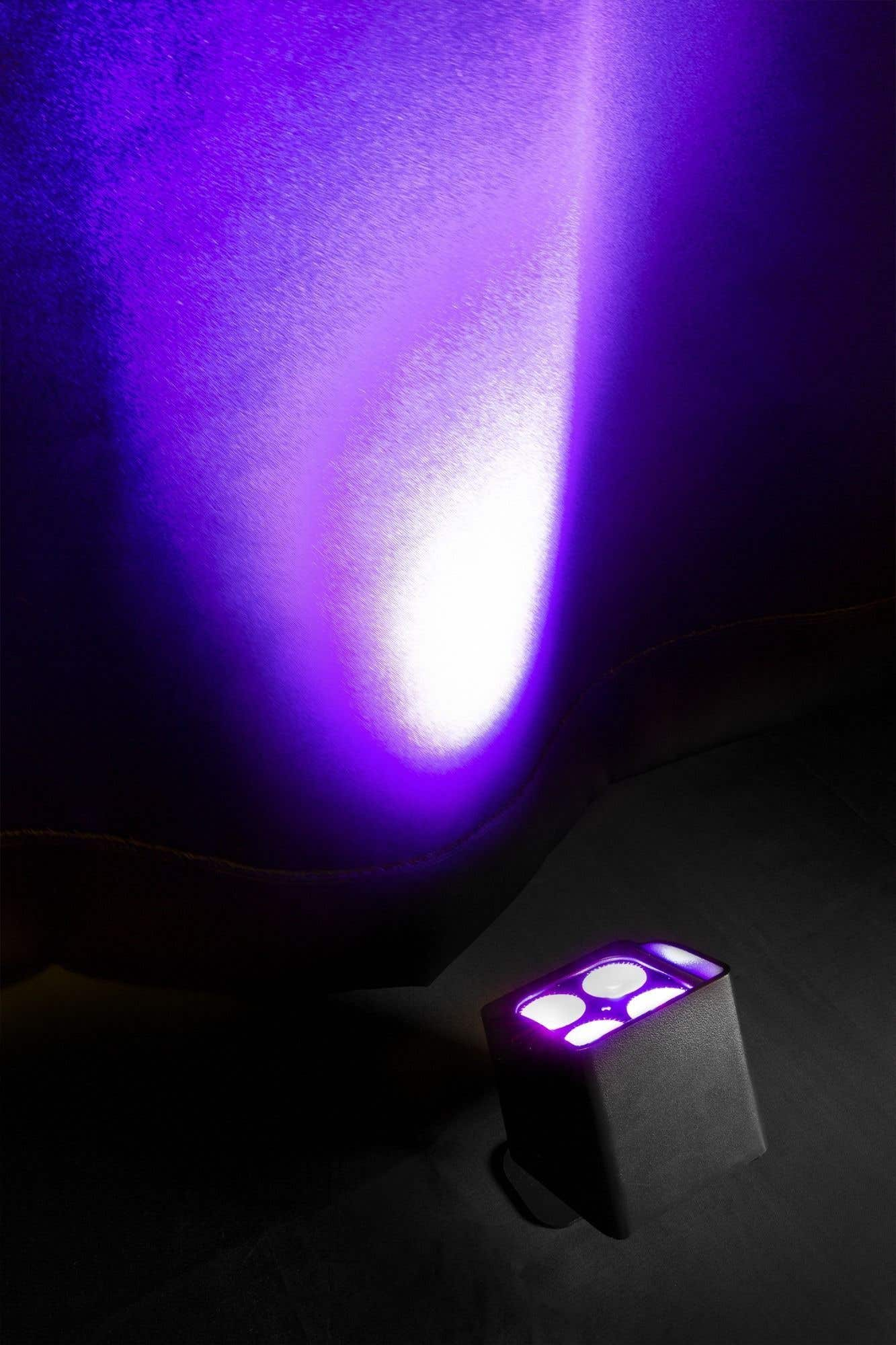 Un projecteur violet illumine une surface sombre. Un luminaire noir avec des lumières violettes brillantes est dans le coin inférieur droit.