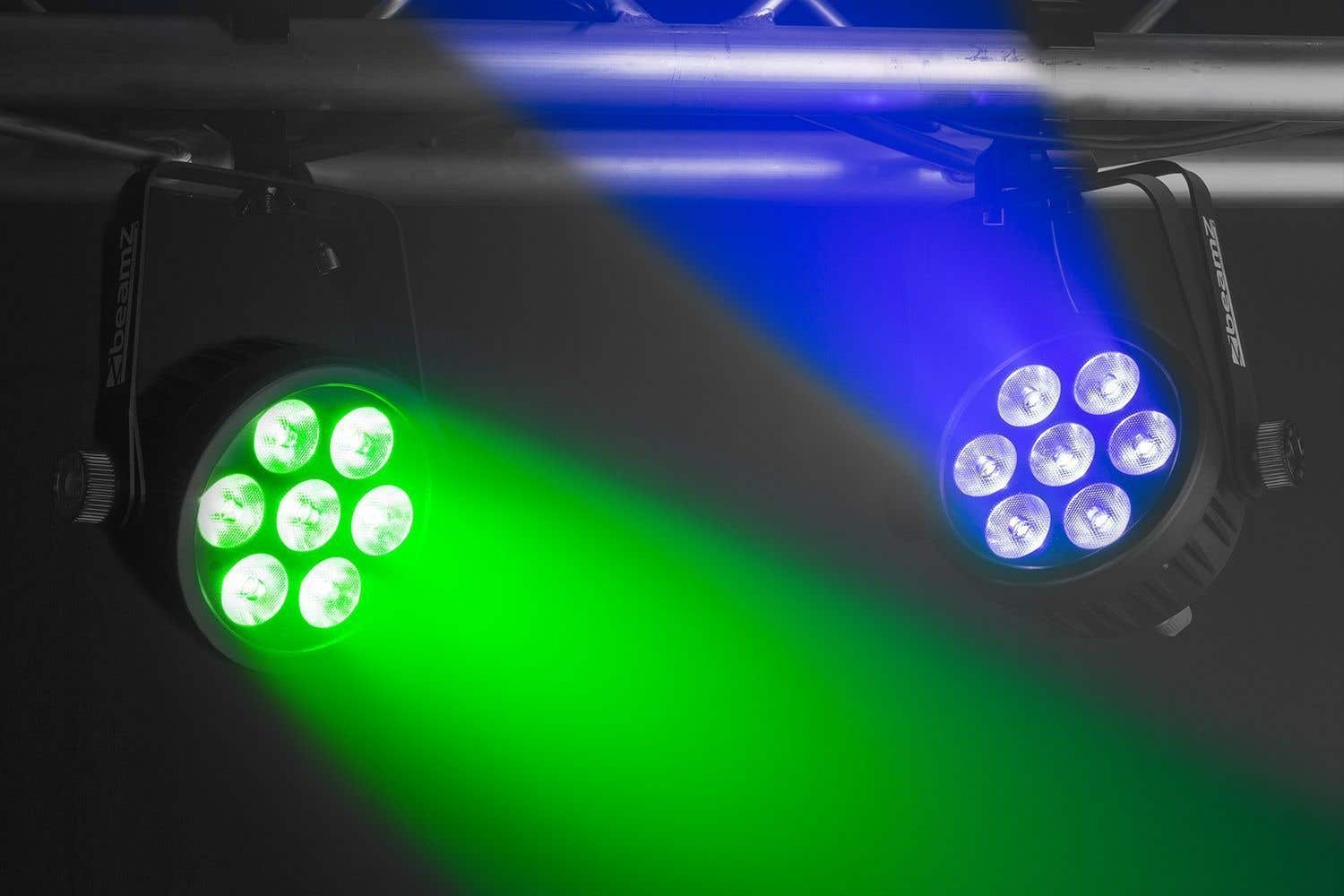 Dos focos de escenario proyectan haces verdes y azules. La luz izquierda brilla en verde, la derecha en azul. Ambos están montados en una barra metálica.