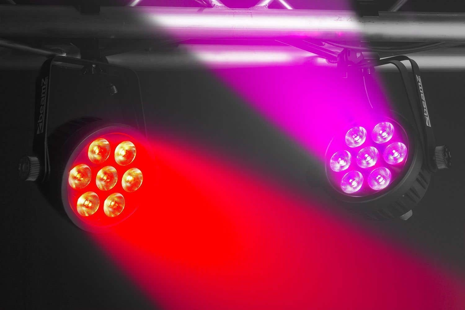 Dos focos de escenario proyectan haces rojos y púrpuras. Las luces están montadas en una estructura metálica, en un ambiente oscuro.