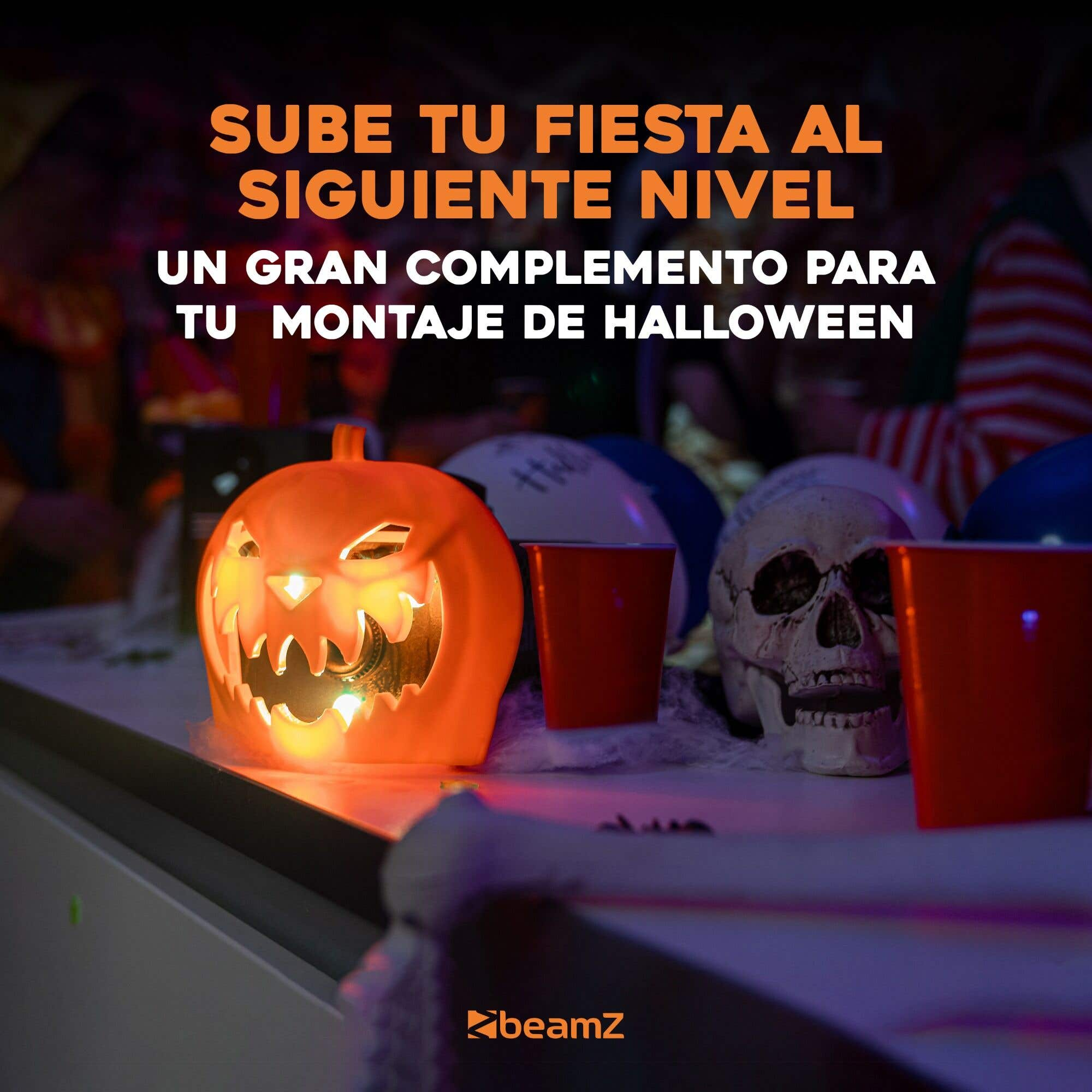 Una calabaza iluminada, una calavera, vasos rojos y texto sobre Halloween en una mesa. El fondo está borroso.