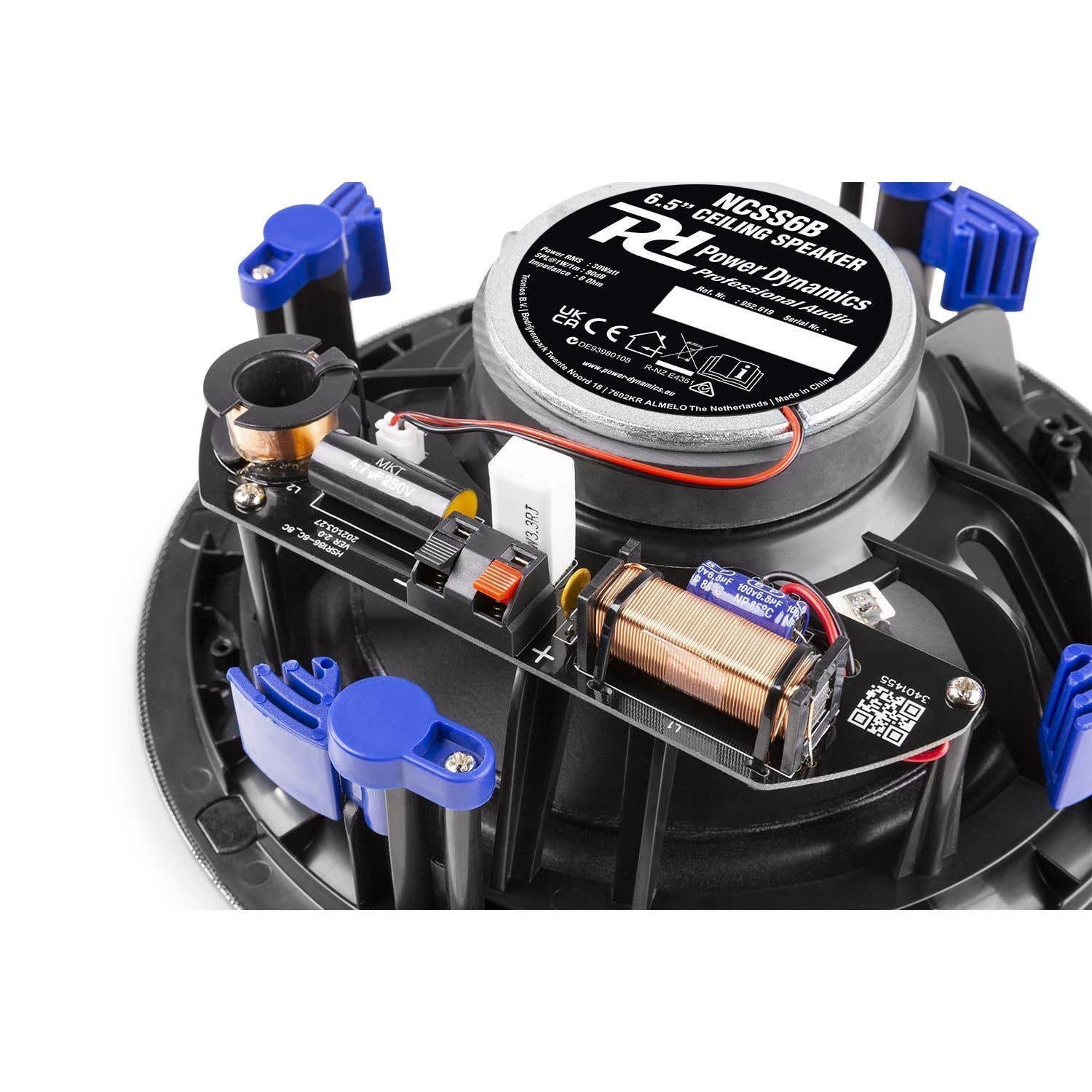 Primer plano de un altavoz de techo con clips azules. Tiene un cuerpo negro y una parte superior plateada con texto. Se ven cables y componentes.
